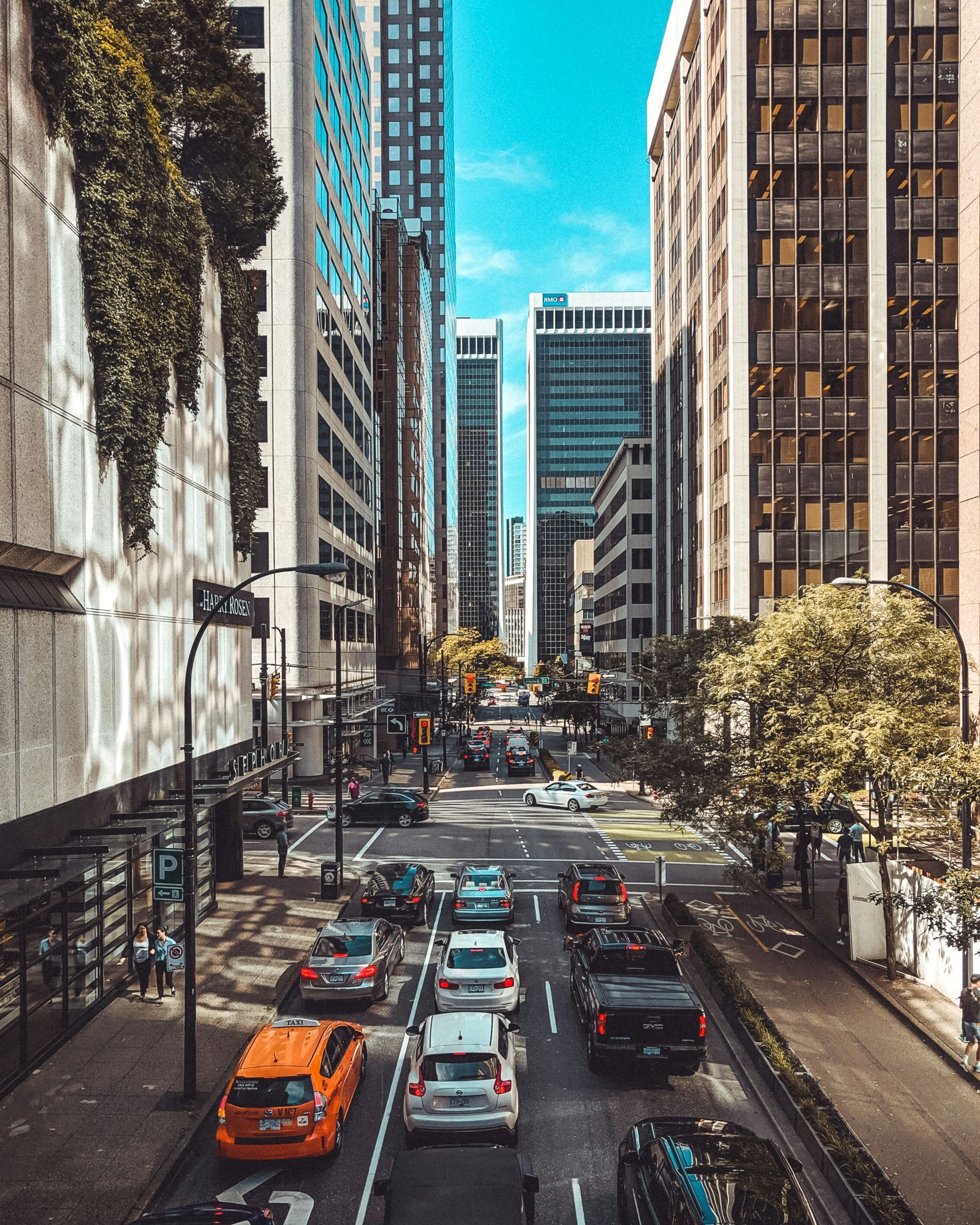 Cars drive down a city street lined with tall buildings in Vancouver, Canada.