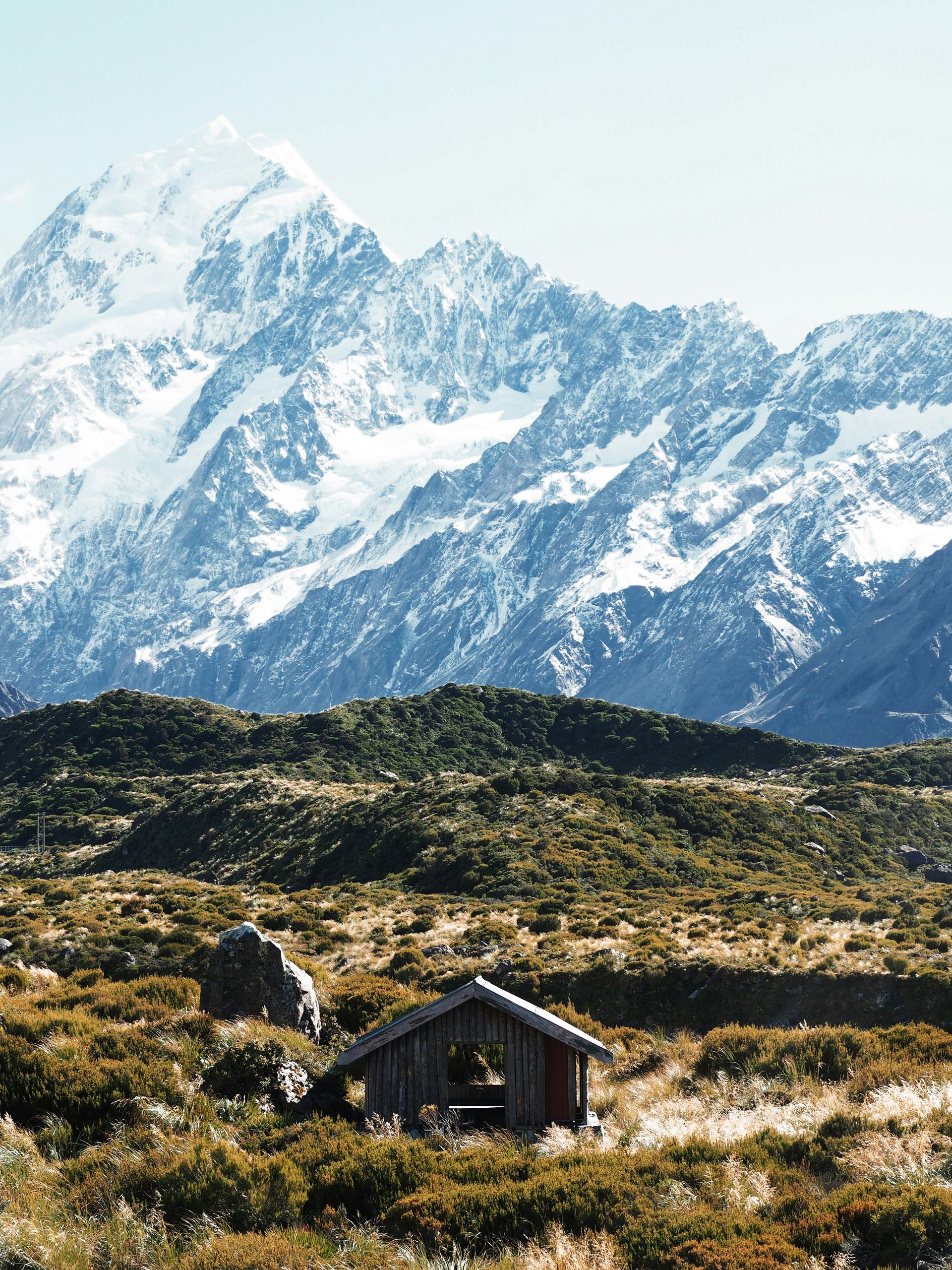 A small hut in the middle of a field with mountains in the background in Mount Cook National Park, New Zealand.