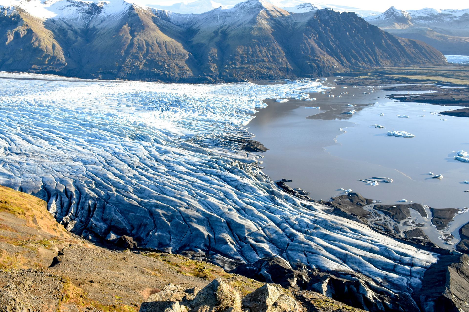 Glacier flows into a lake, mountains in the background. Snowy peaks, icy blue water at Vatnajökull National Park, Iceland.