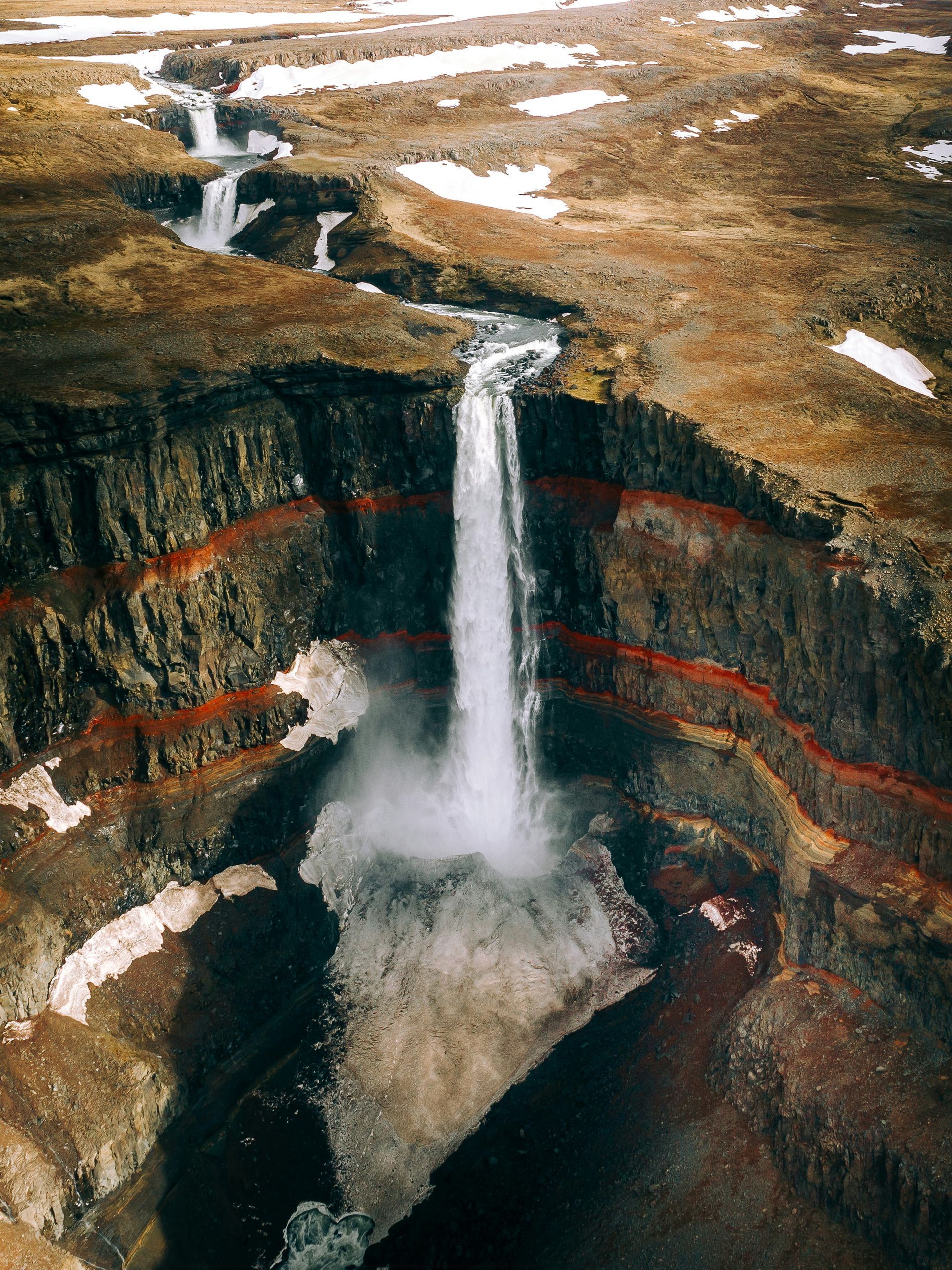 The Hengifoss Waterfall cascades into a canyon with visible red rock layers in Iceland.