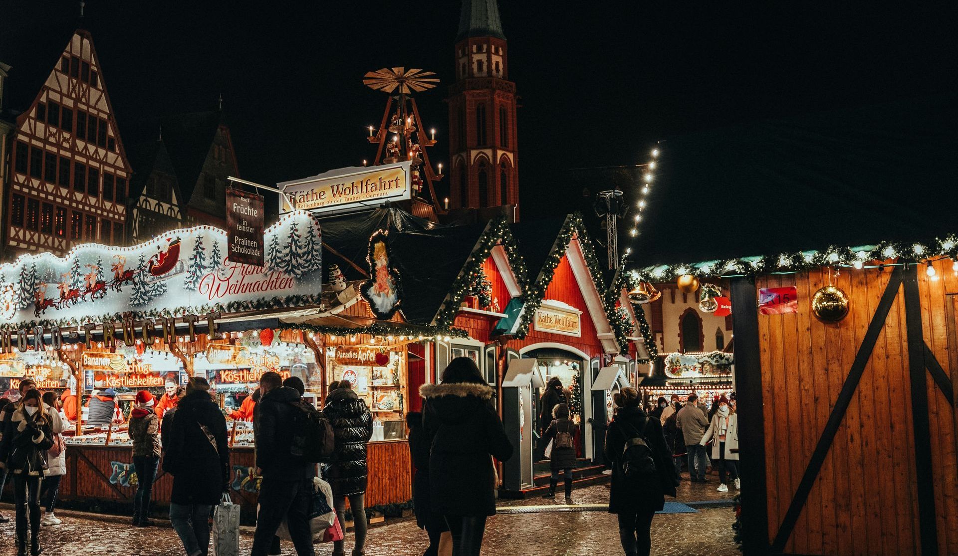 A group of people are walking through a Christmas market in Germany at night.