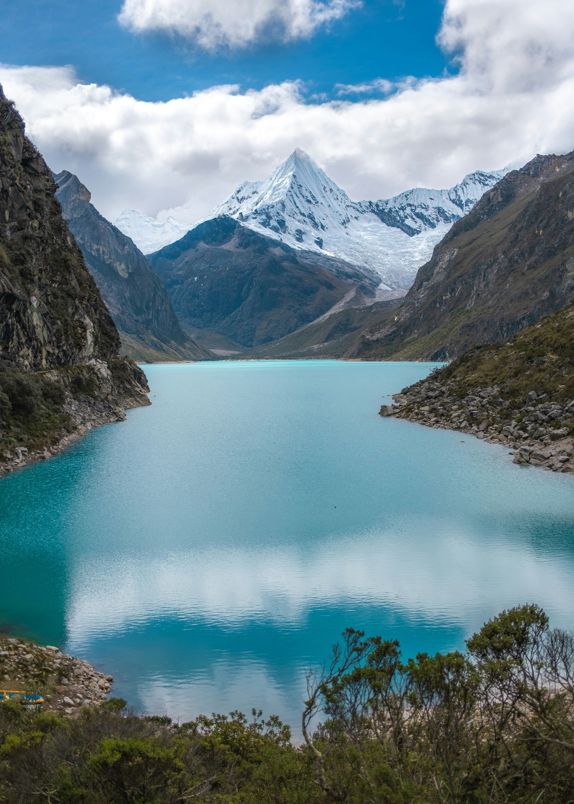 Lake Paron surrounded by snow covered mountains on a sunny day in Huascarán, Peru.