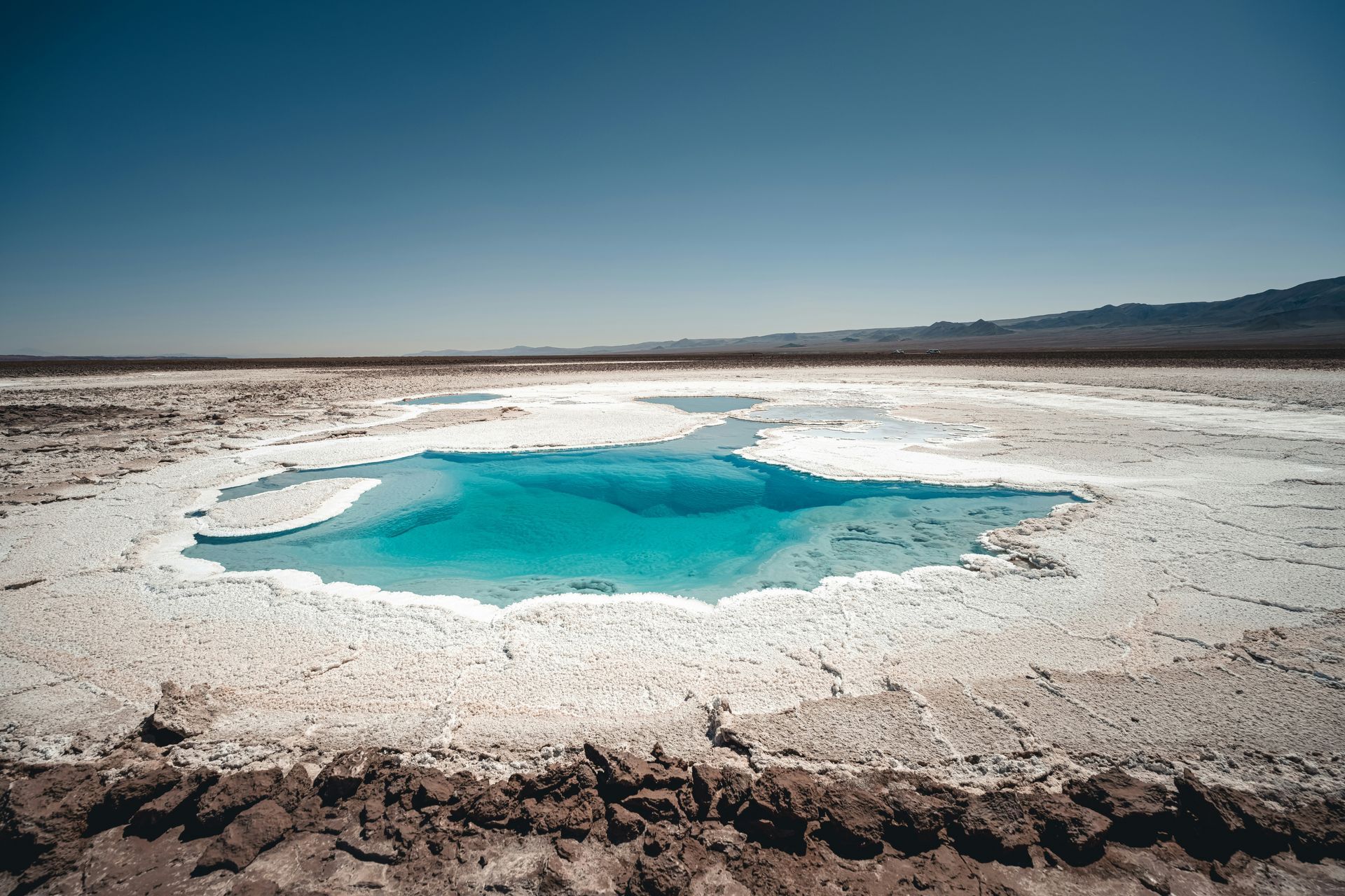 Bright turquoise water in a salt flat, surrounded by white salt and arid landscape in the Atacama Desert, Chile.