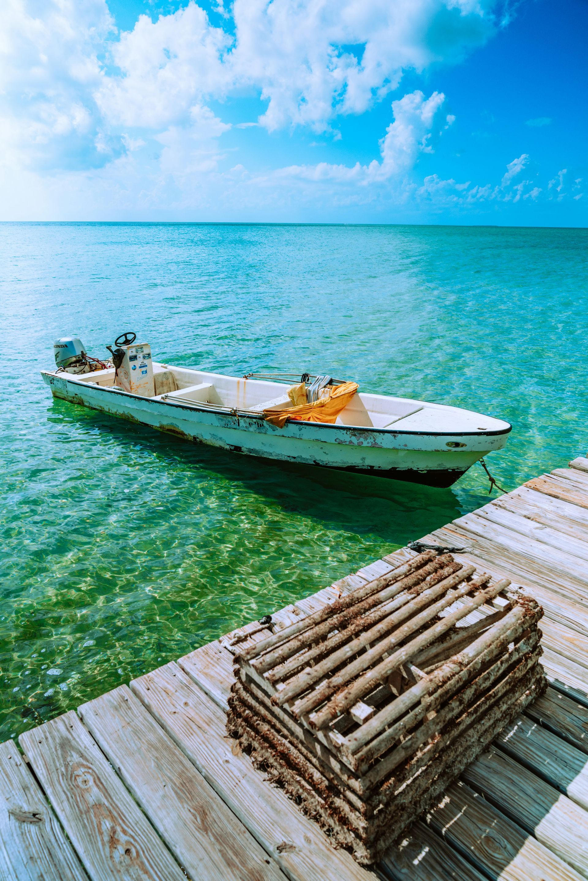 Boat floats in turquoise water near a wooden dock; lobster traps rest on the dock, in Ambergris Caye, Belize.