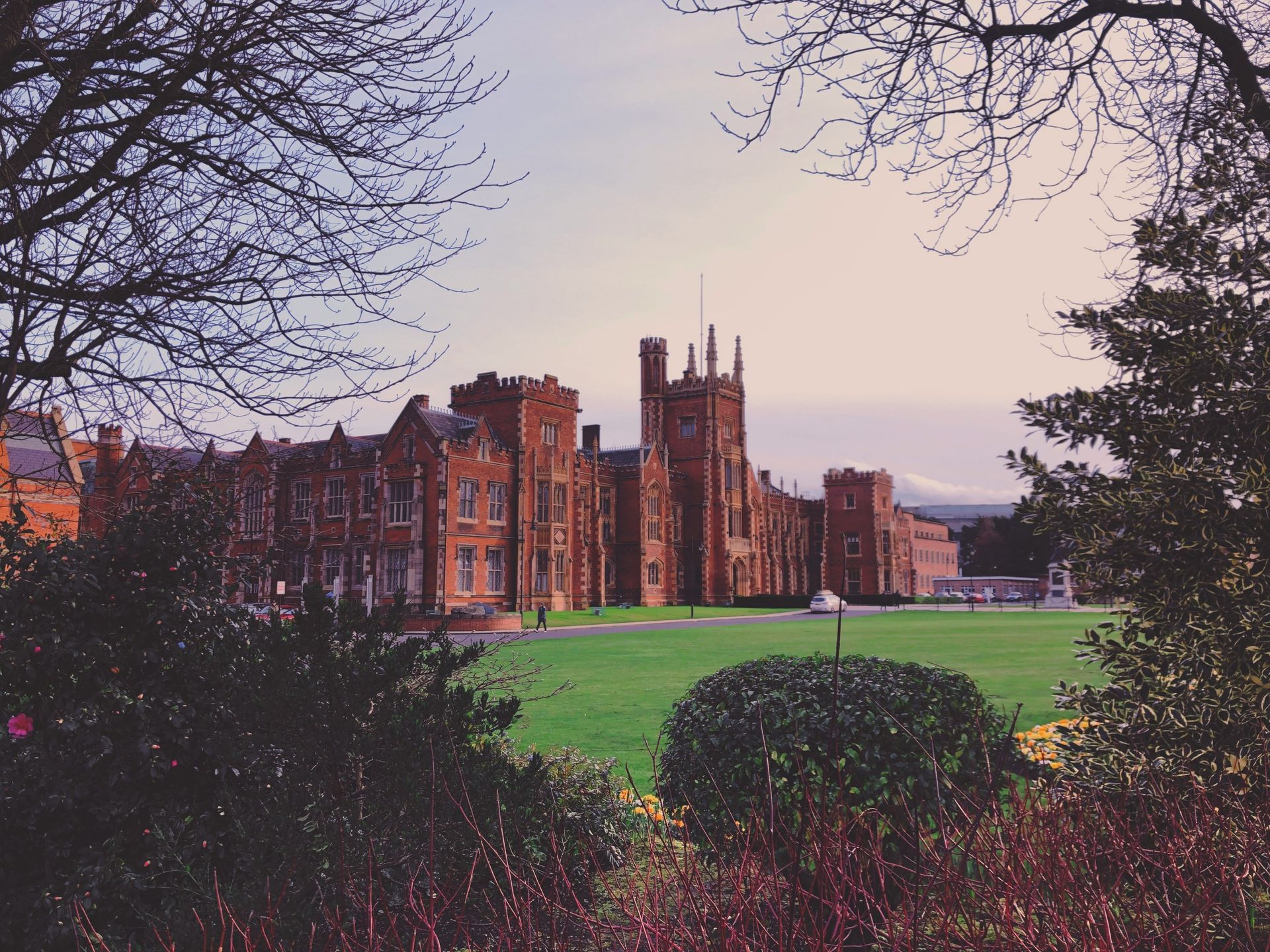 Red brick university building framed by trees on a green lawn.