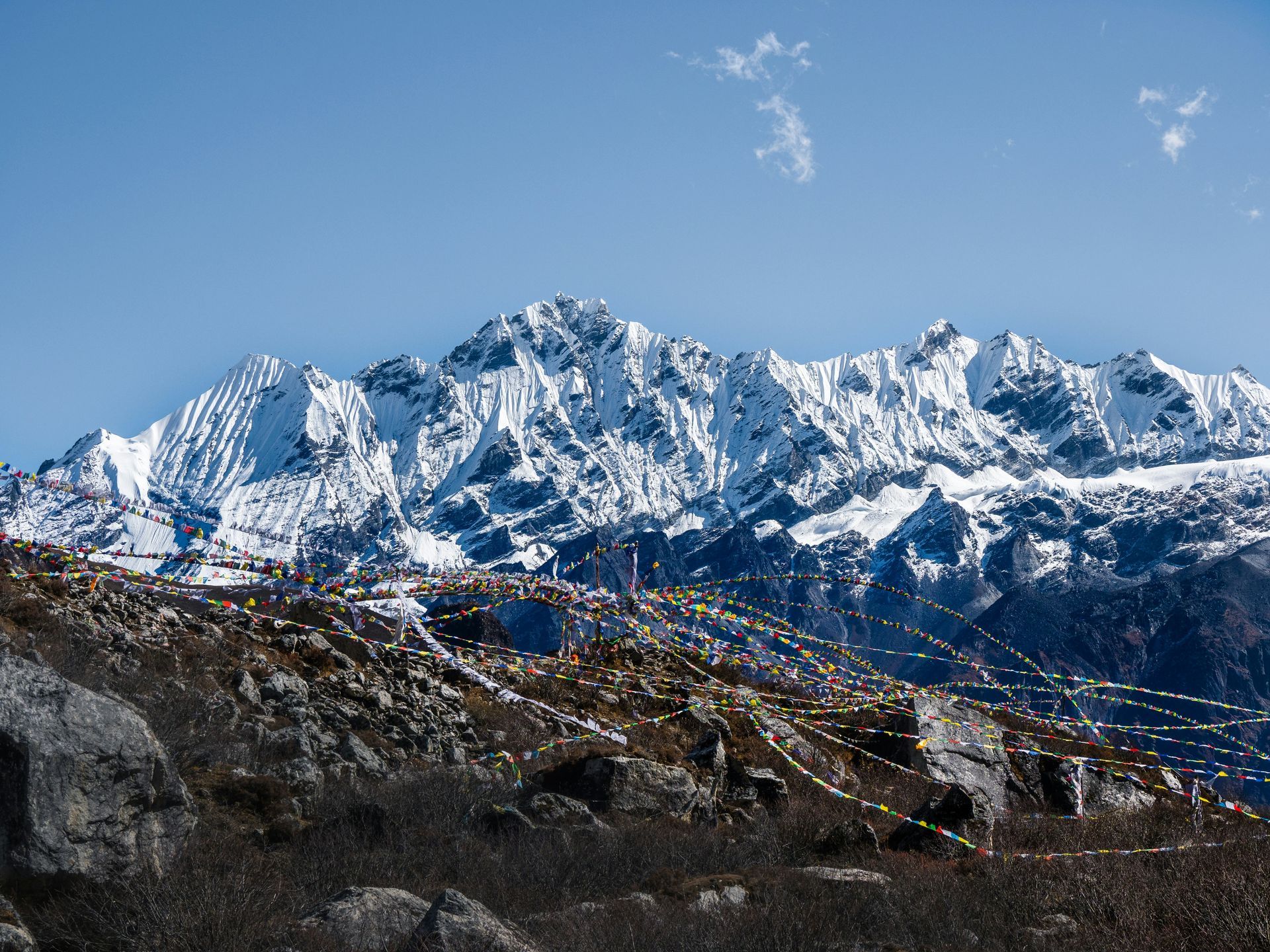 Snow-covered mountain range under a blue sky, prayer flags in the foreground in Langtang, Nepal.