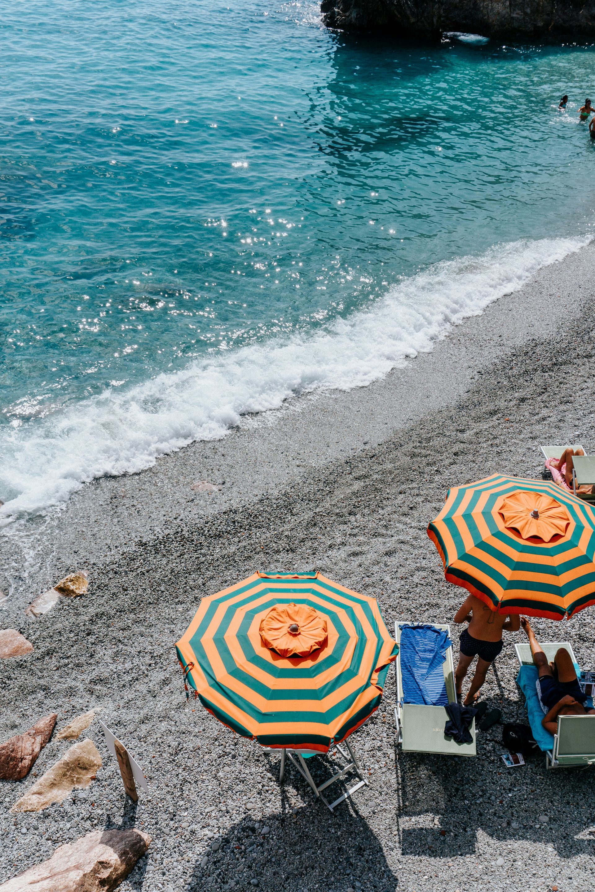 A group of people are sitting under umbrellas on a beach in Cinque Terre, Italy.