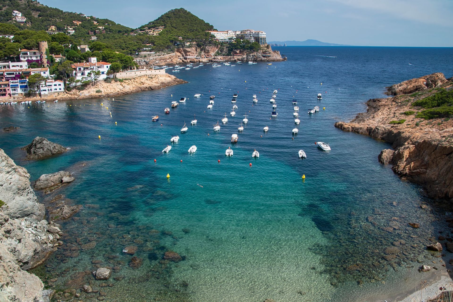 There are many boats in the water near the shore on Costa Brava, Spain.