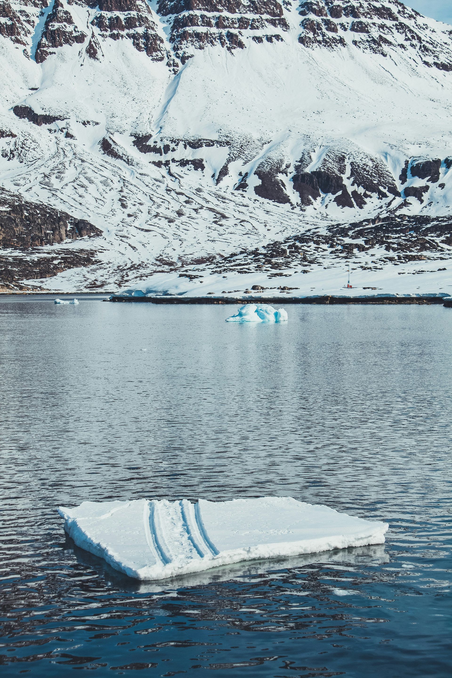 Snowy mountain overlooks icy water with ice floe in Disko Bay, Greenland.