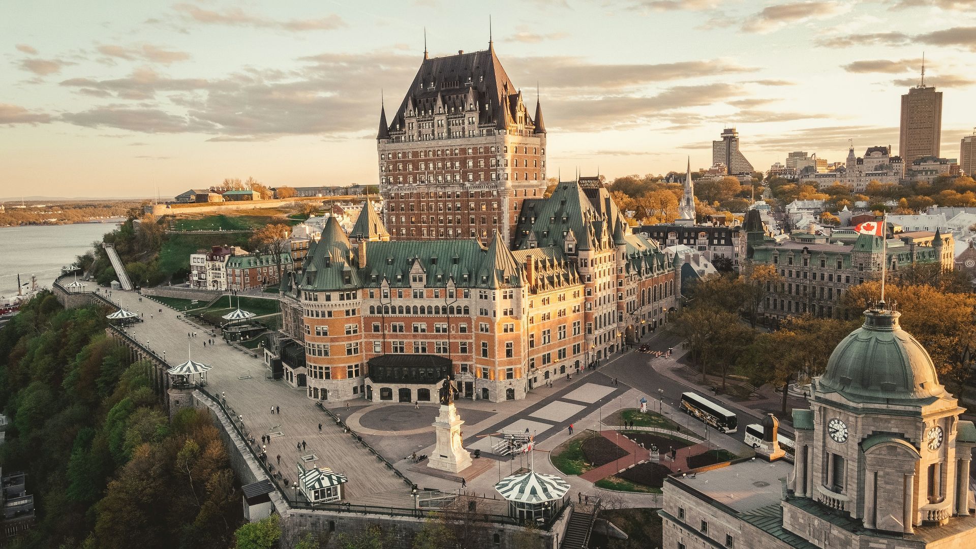 Fairmont Le Château Frontenac, a large castle, overlooks Quebec City. A tree-lined path and river are in the foreground.