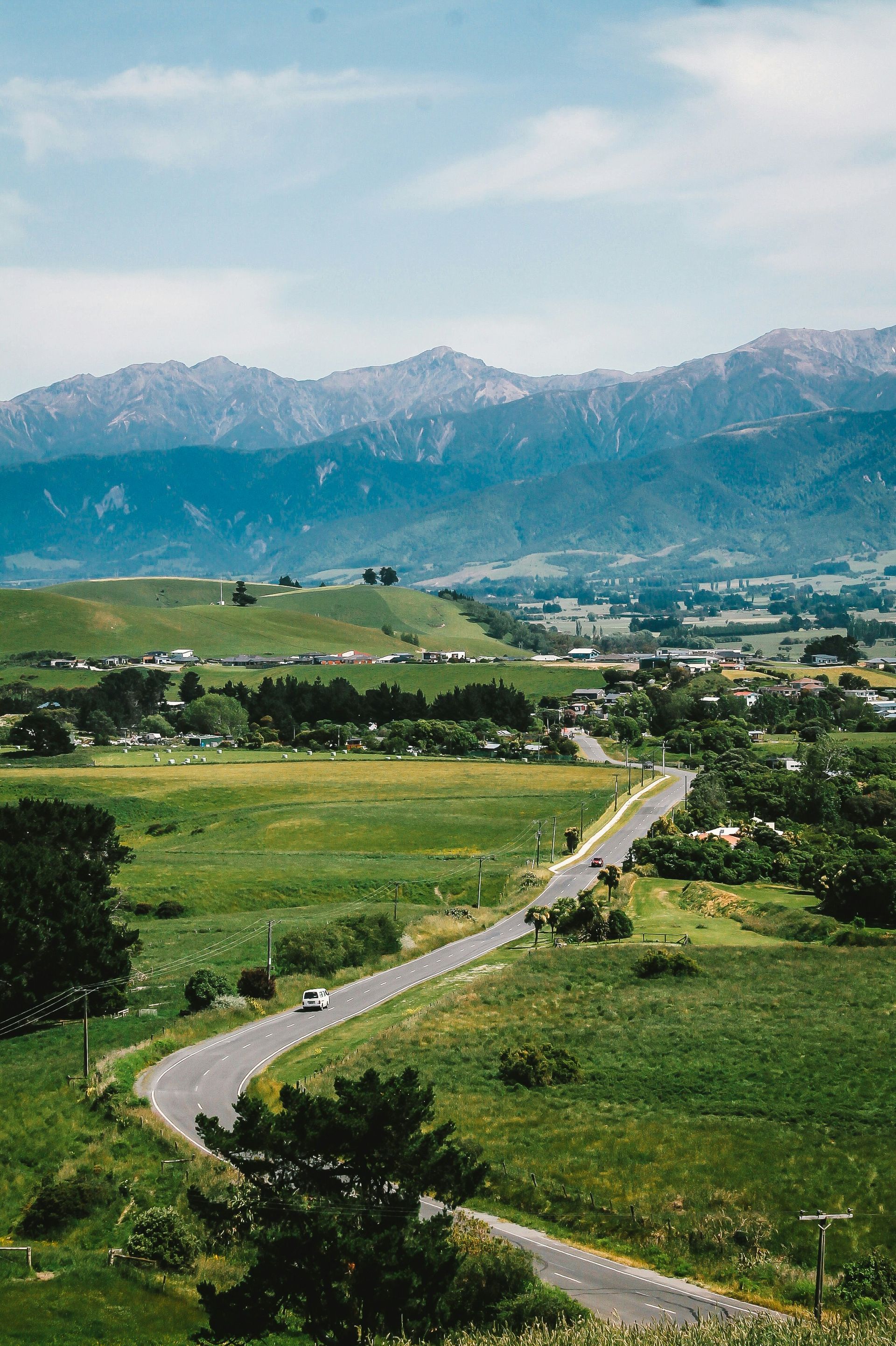 A road going through a grassy field with mountains in the background in Kaikōura, New Zealand.