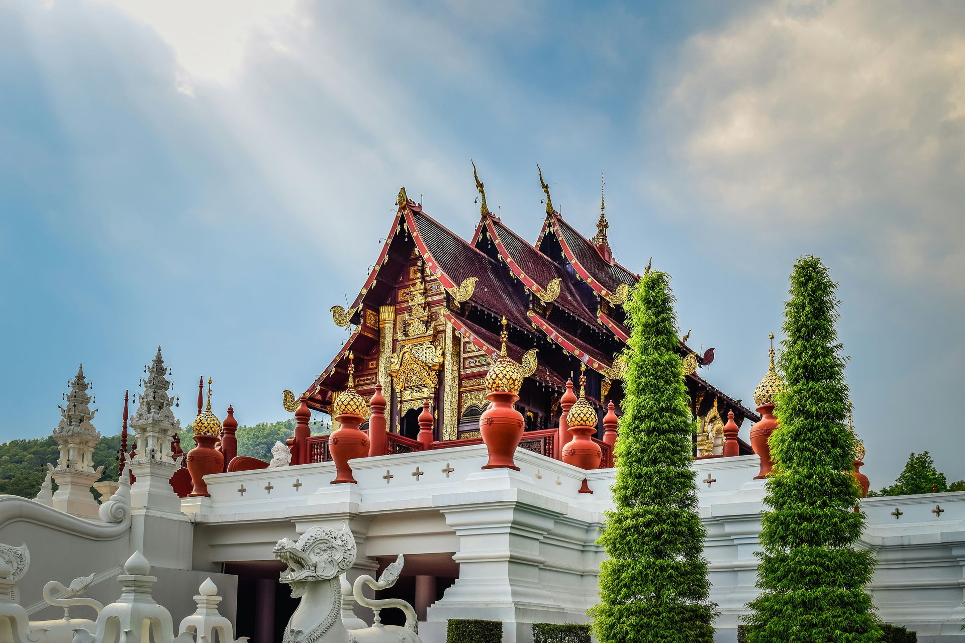 A temple with a lot of statues on the roof and trees in front of it in Chiang Mai, Thailand.