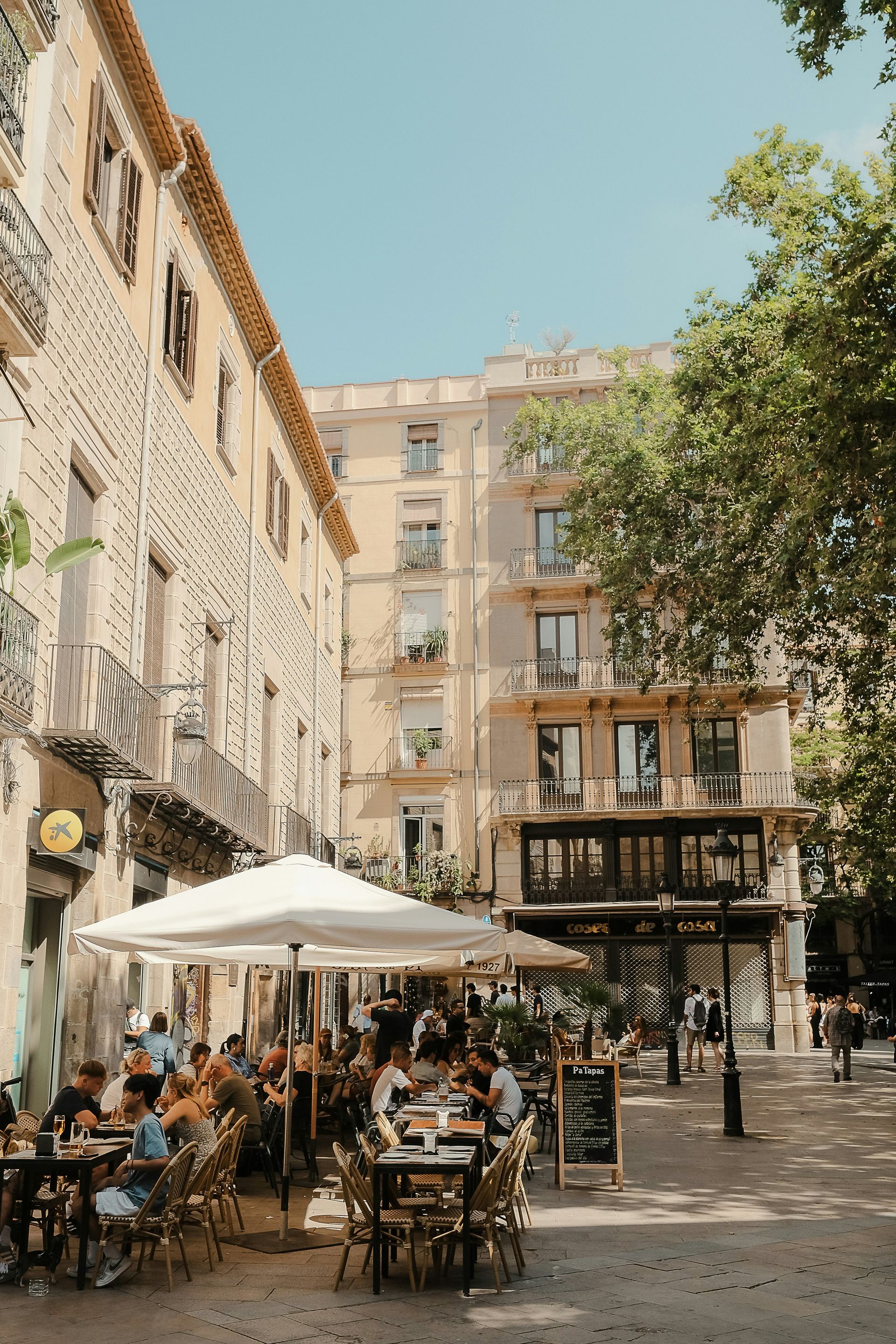 Outdoor cafe with people, tables, and umbrellas, with buildings in the background in Barcelona, Spain.