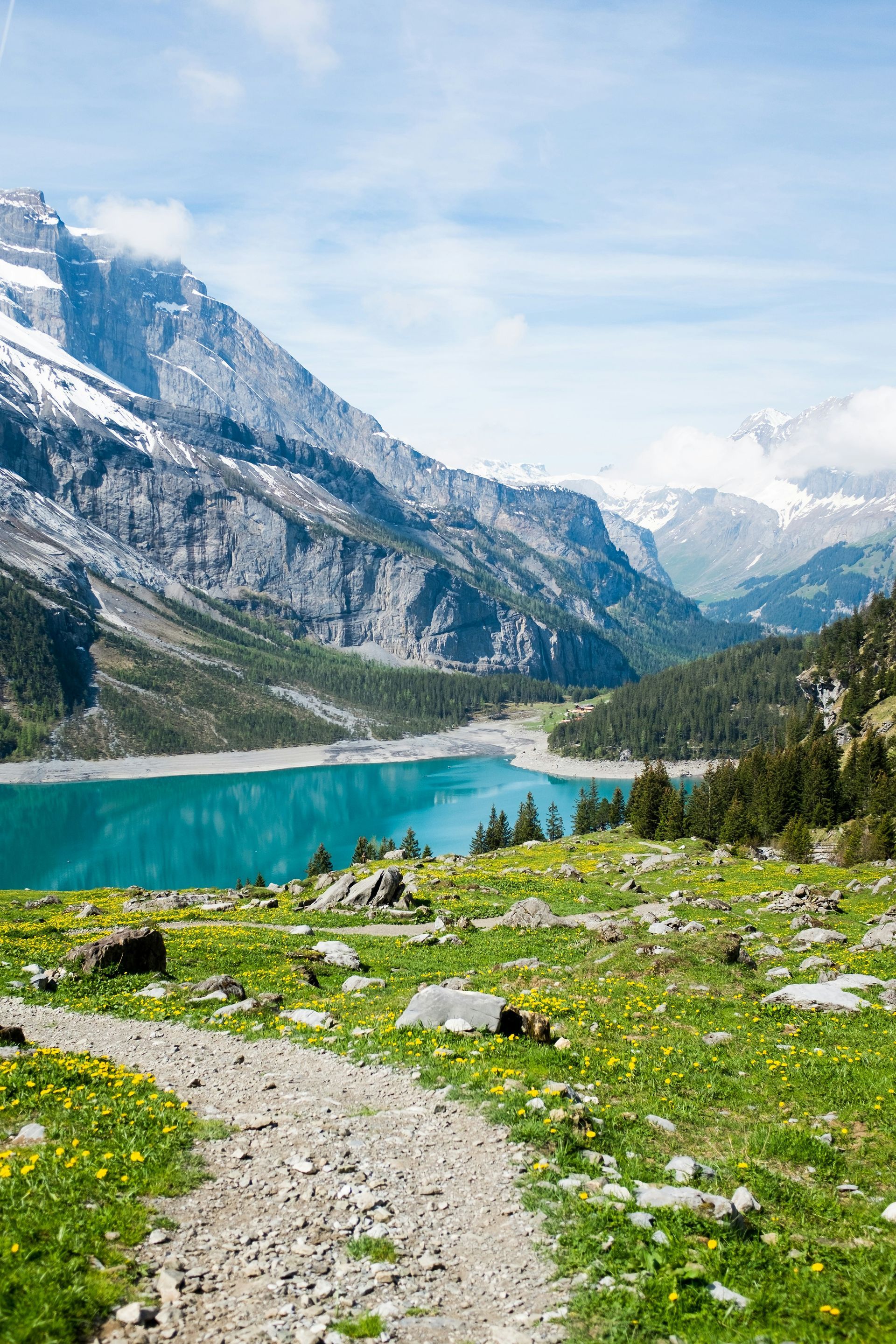 The turquoise Lake Oeschinensee is nestled between mountains and a meadow with a hiking path in Kandersteg, Switzerland.