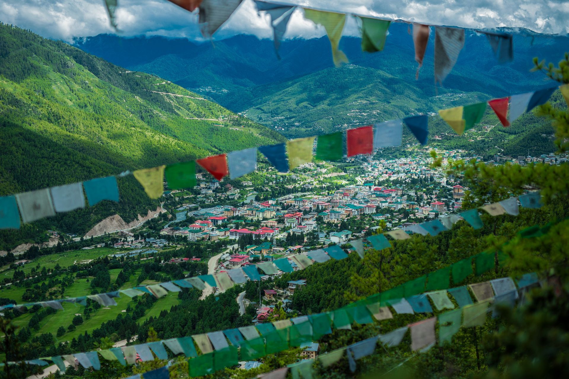 View of Thimphu, Bhutan, from hillside; colorful prayer flags; green mountains.