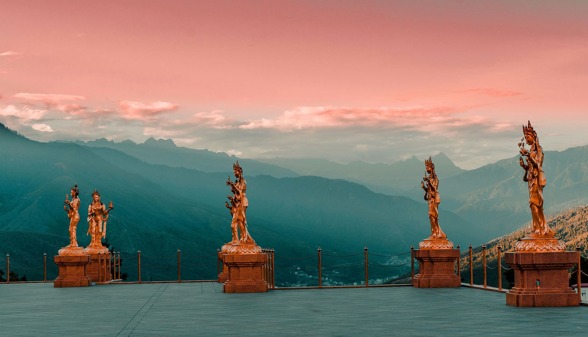 Golden statues on a platform overlooking a mountain range at sunset in Thimphu, Bhutan.