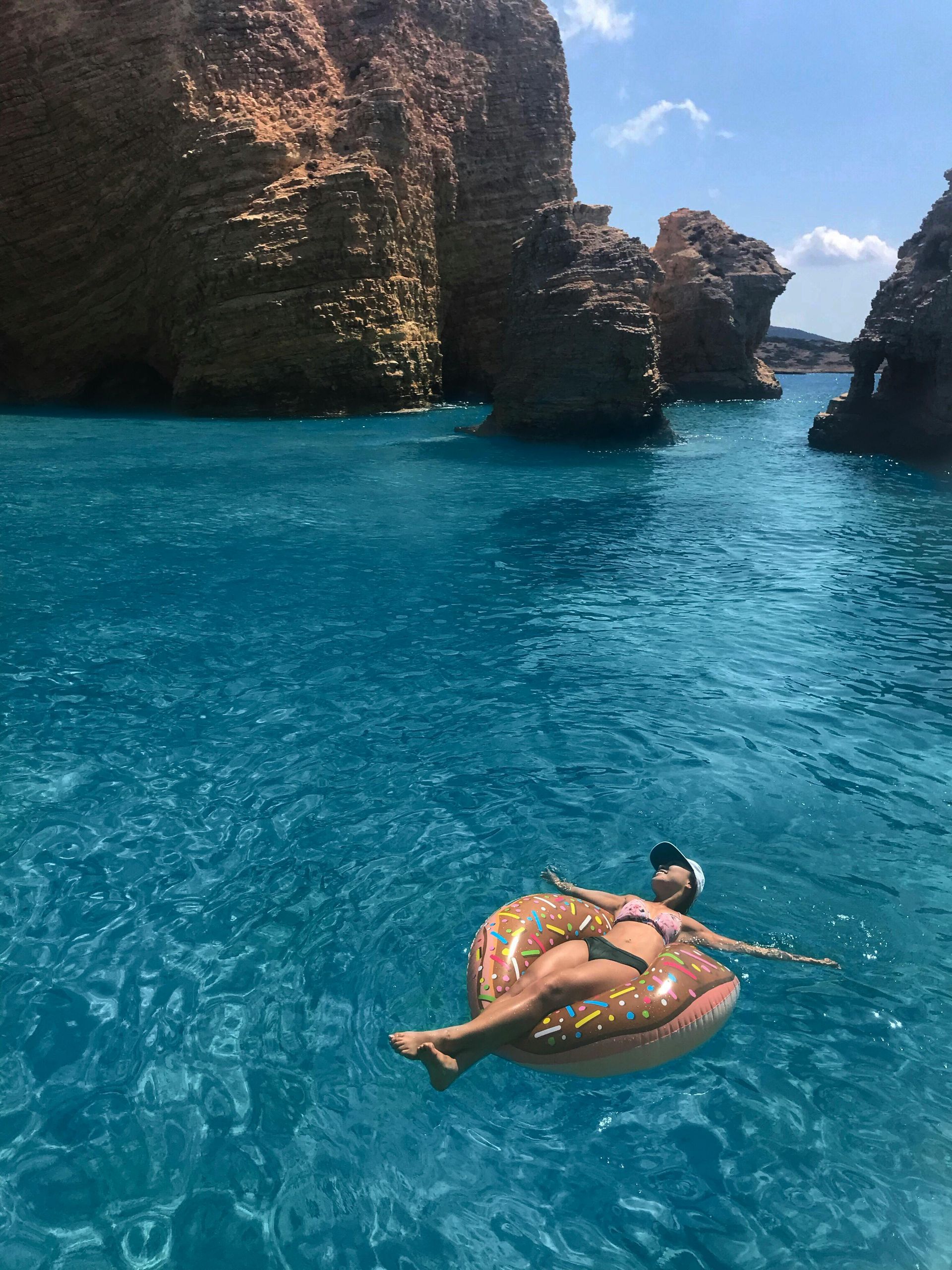 A woman is floating on a donut float in the ocean in Paros, Greece.