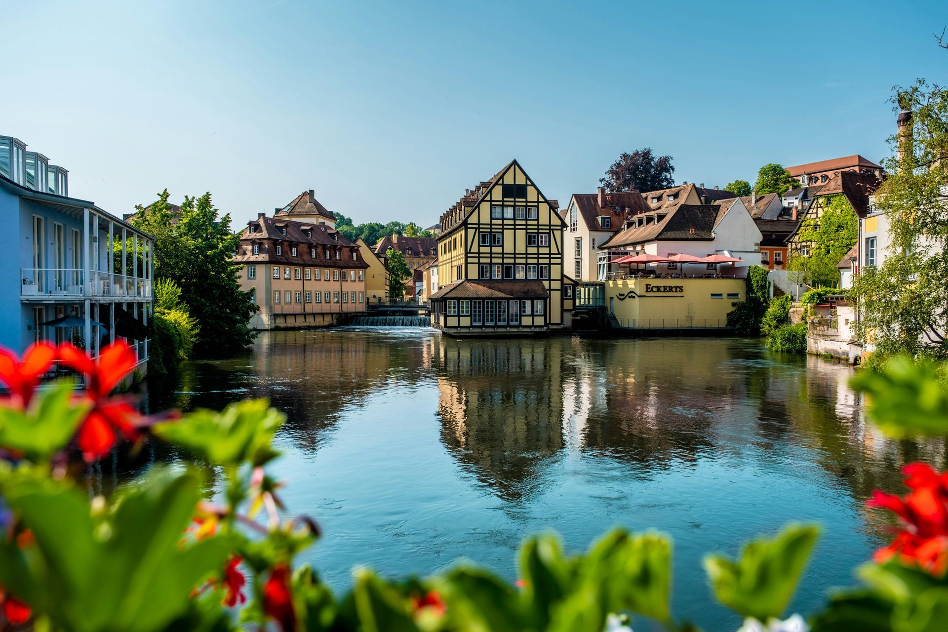 A river runs through a small town of Bamberg, Germany surrounded by buildings and flowers.