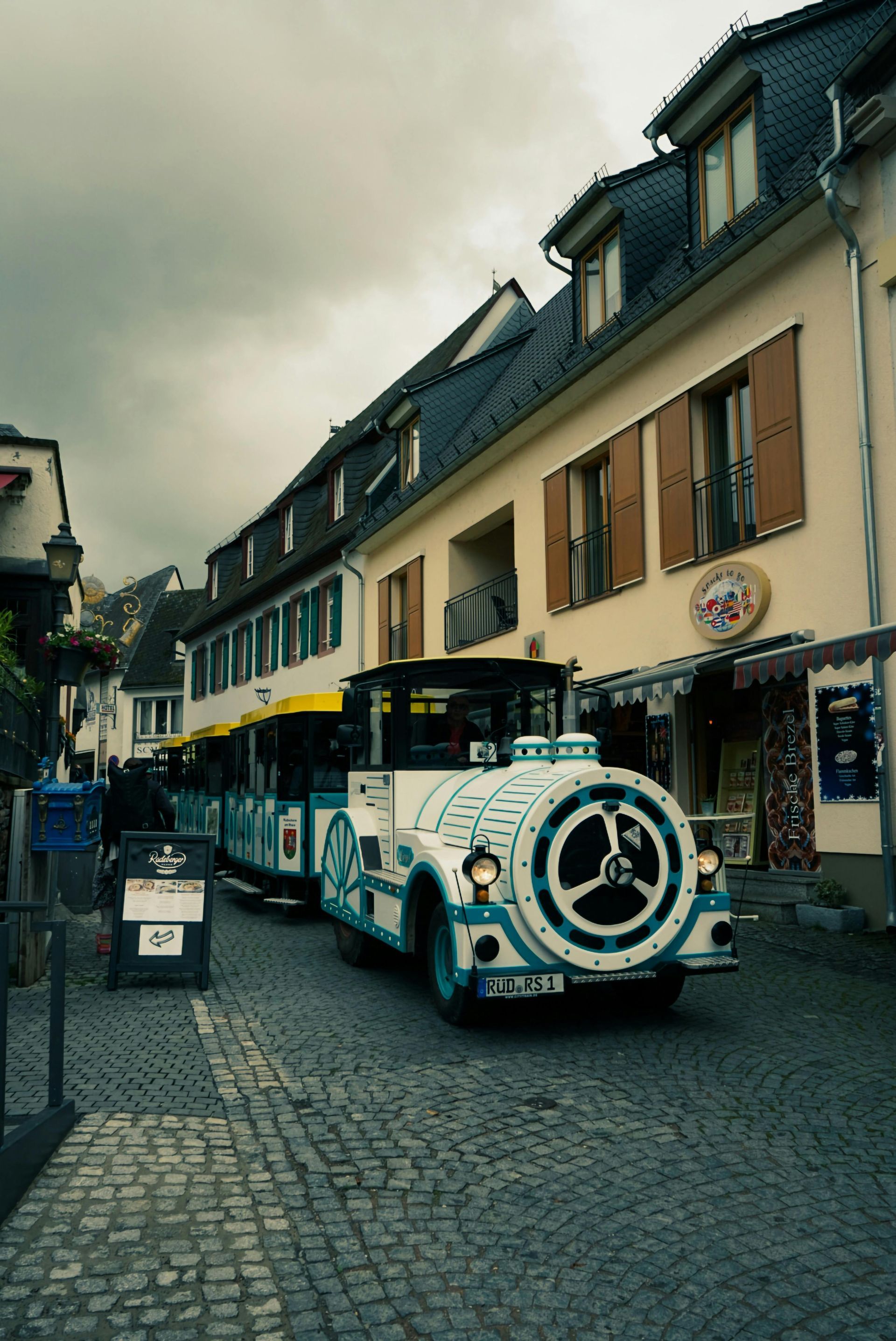 A blue and white train is driving down a cobblestone street in Rudesheim, Germany.