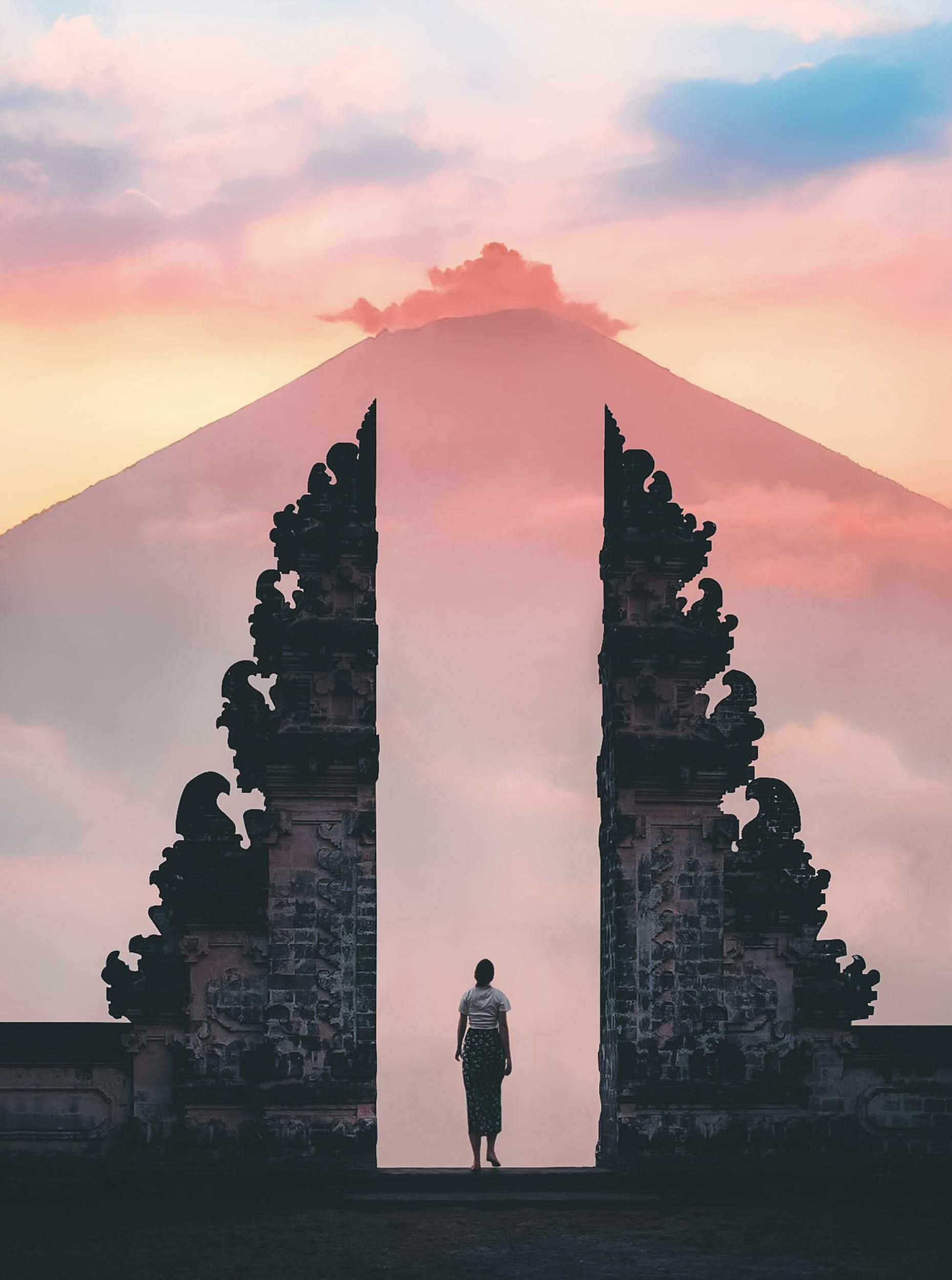 A man is standing in front of a gate with a mountain in the background in Bali.