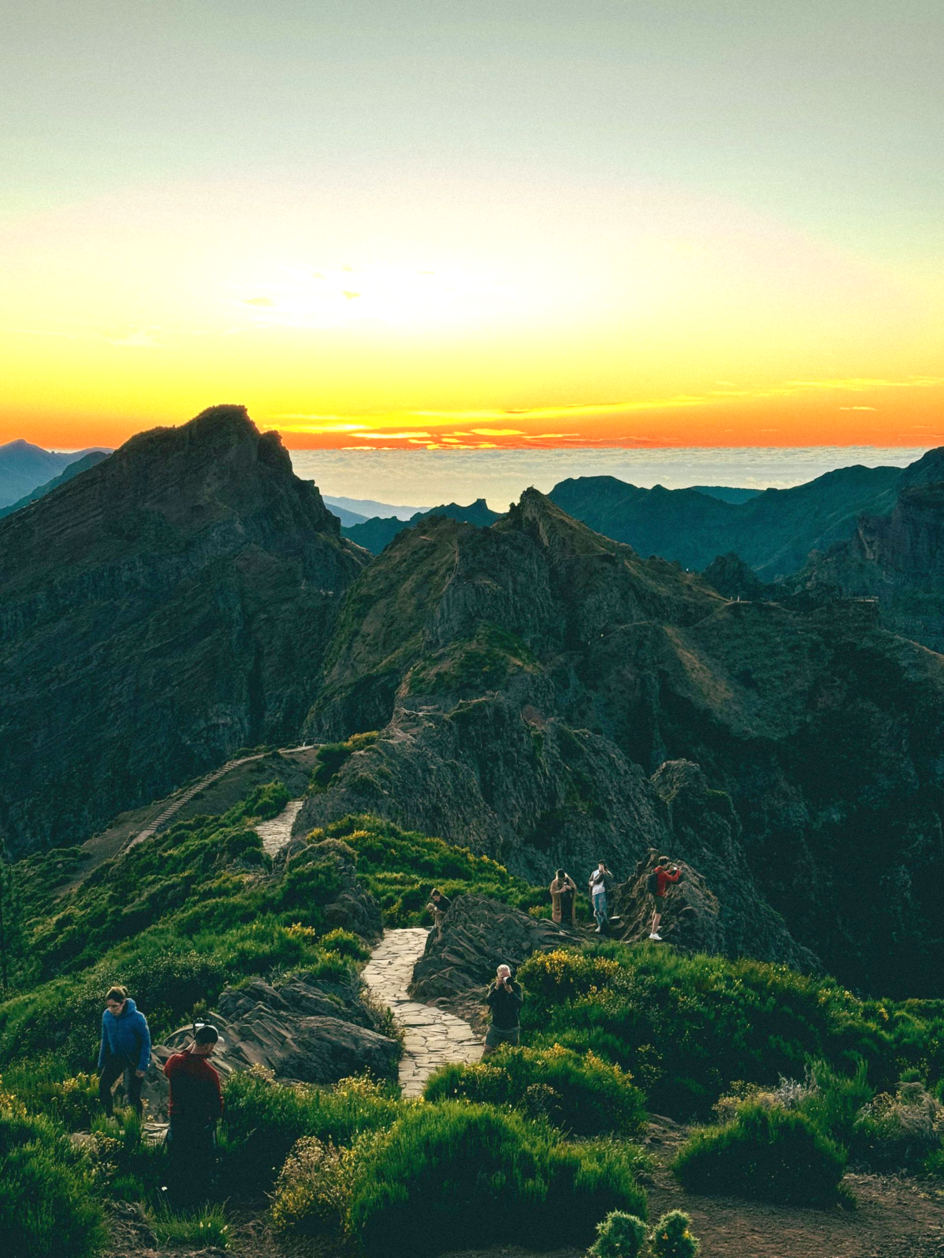 Mountain trail at sunrise with hikers silhouetted against the vibrant sky and rocky peaks on the island of Madeira, Portugal.