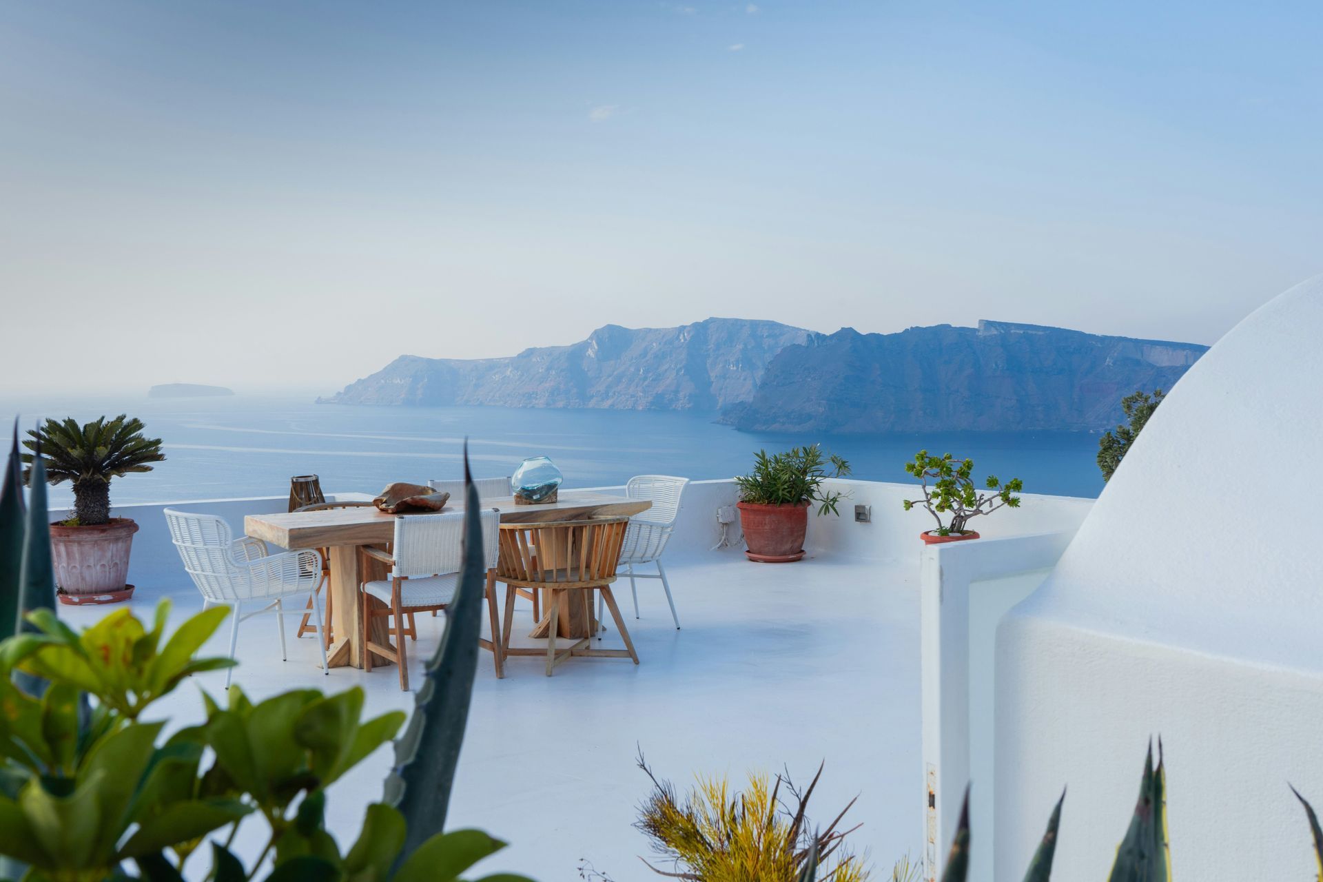 There is a table and chairs on the roof overlooking the ocean in Santorini, Greece.