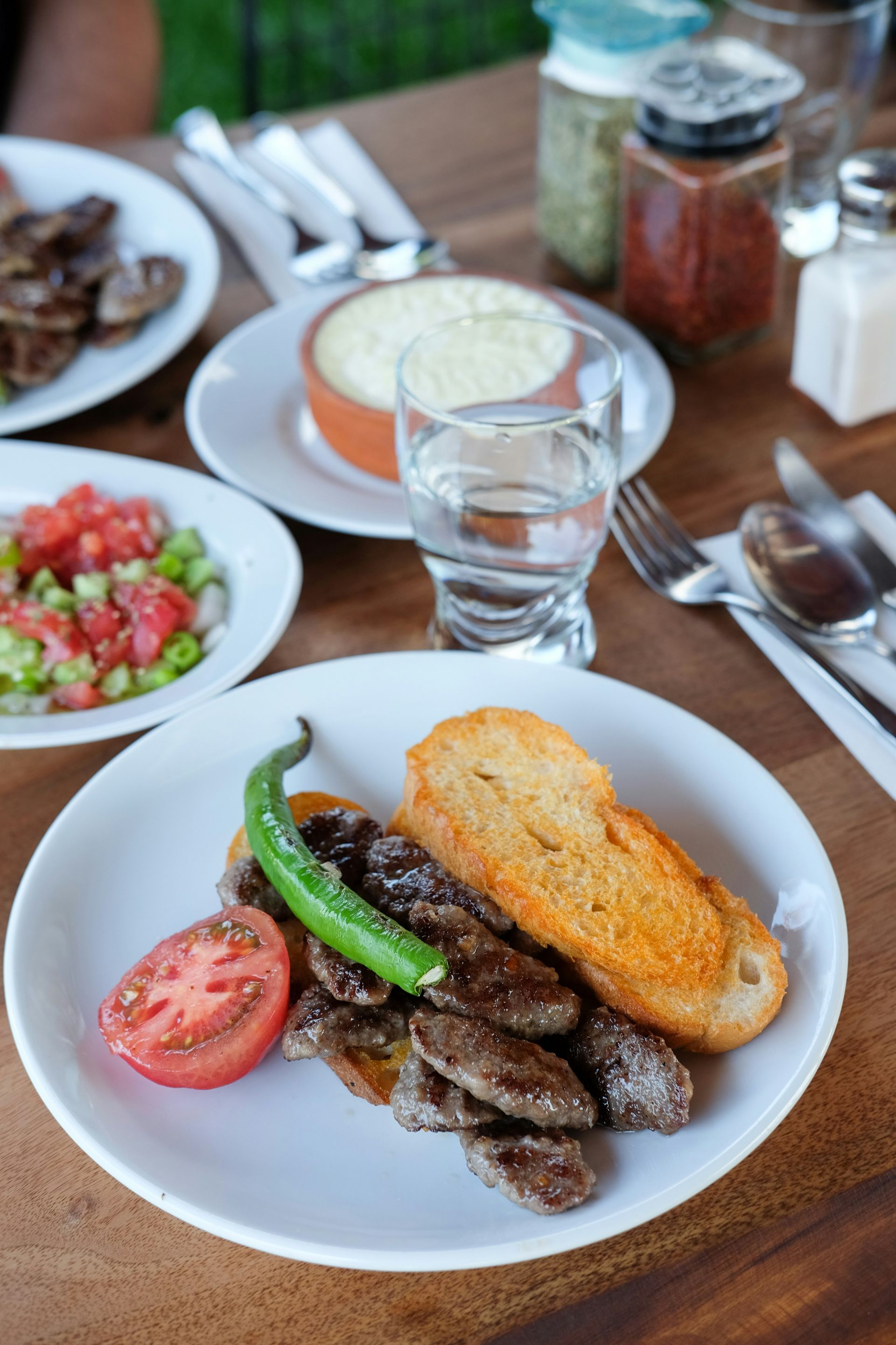 Plate of meatballs, tomato, pepper, and toast with sides of salad and dip on a wooden table in Turkey.
