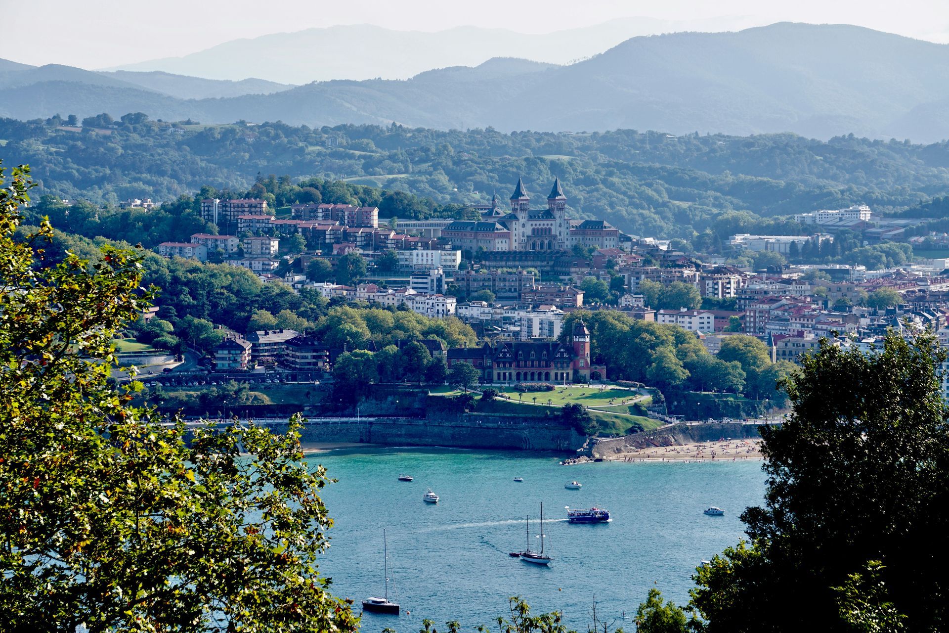Coastal view of San Sebastián, Spain  with buildings on a hillside, bay with boats, and distant mountains.