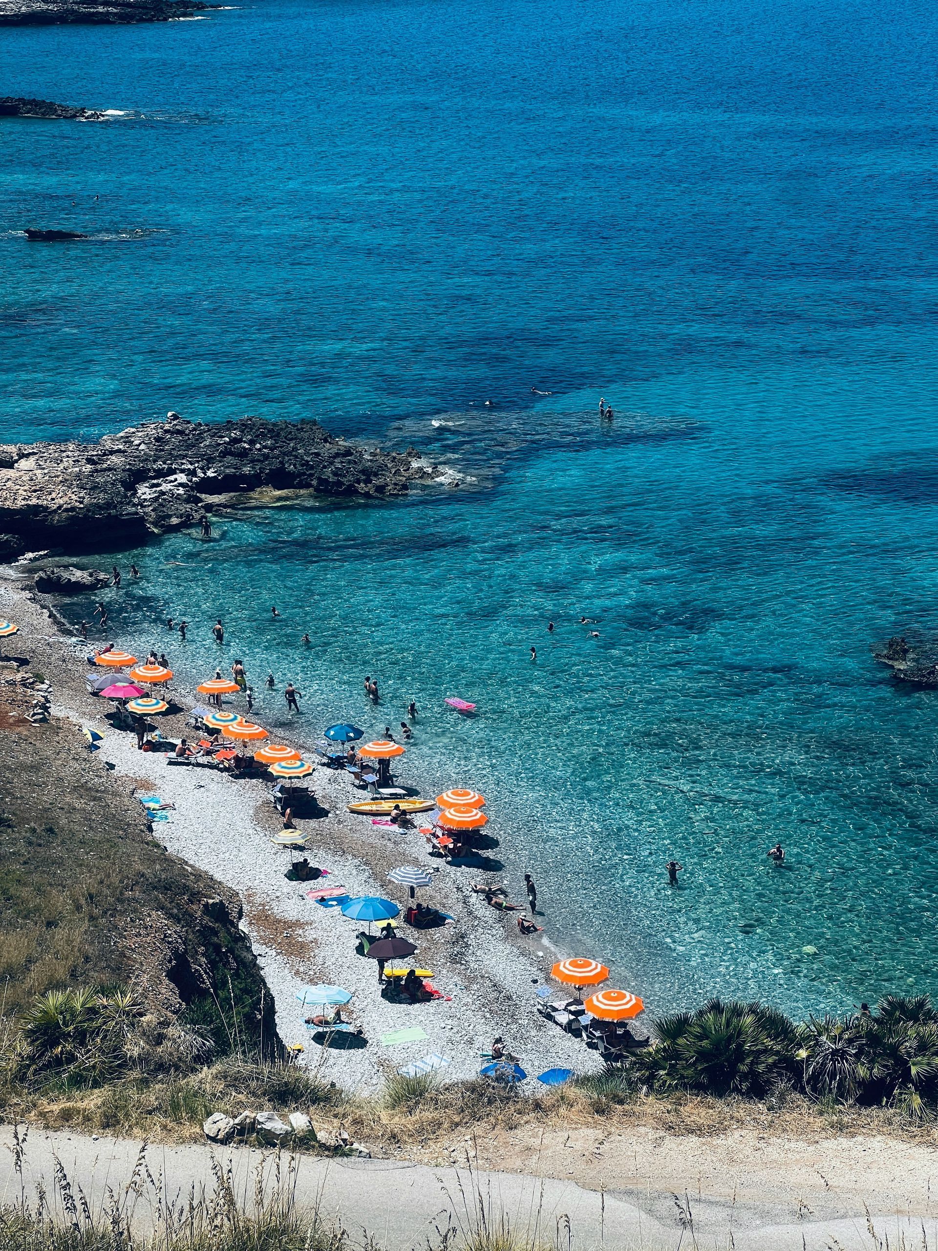 A beach with umbrellas and people swimming in the water in Sicily.