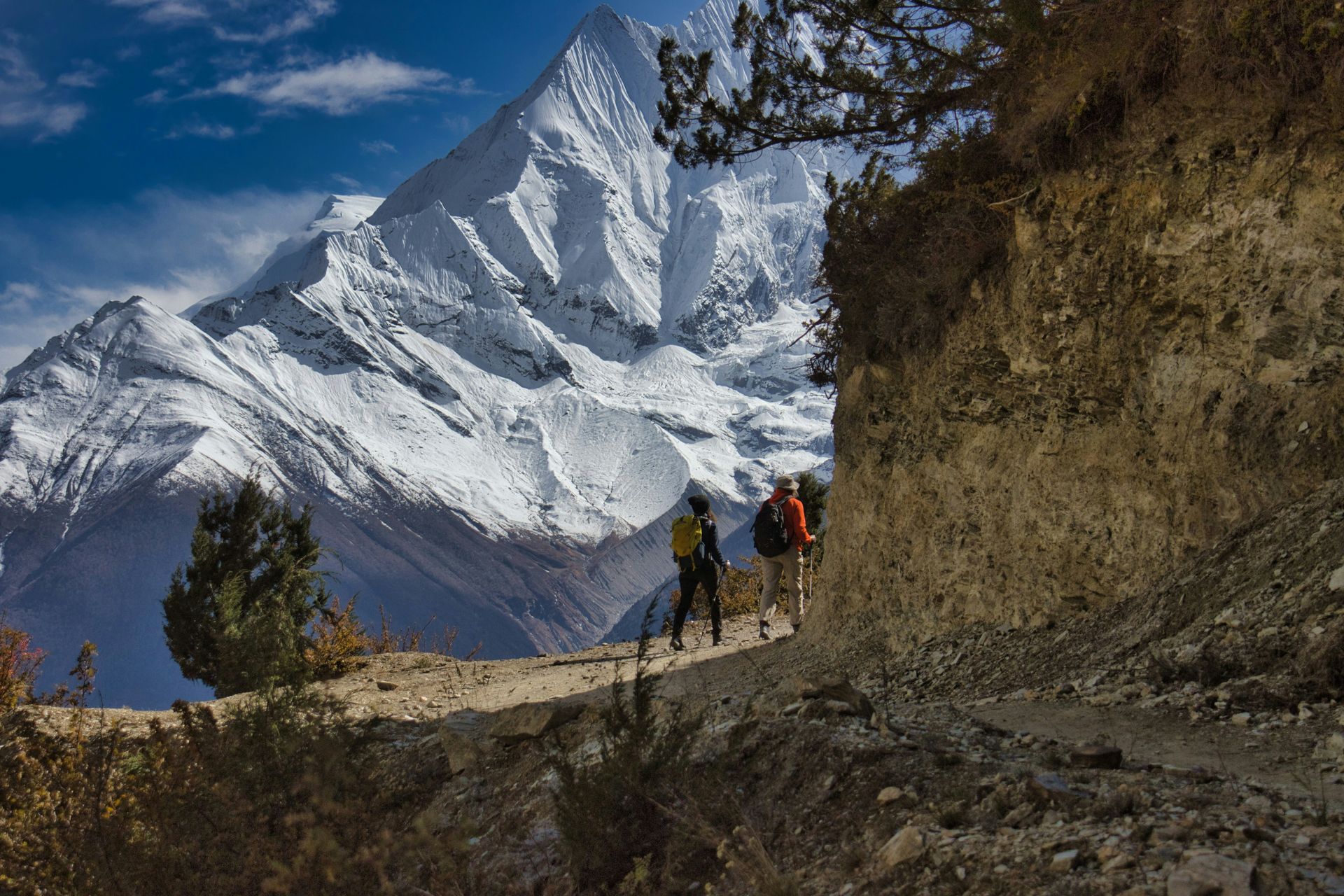 Hikers on a mountain trail with a large snow-covered peak in Annapurna, Nepal.