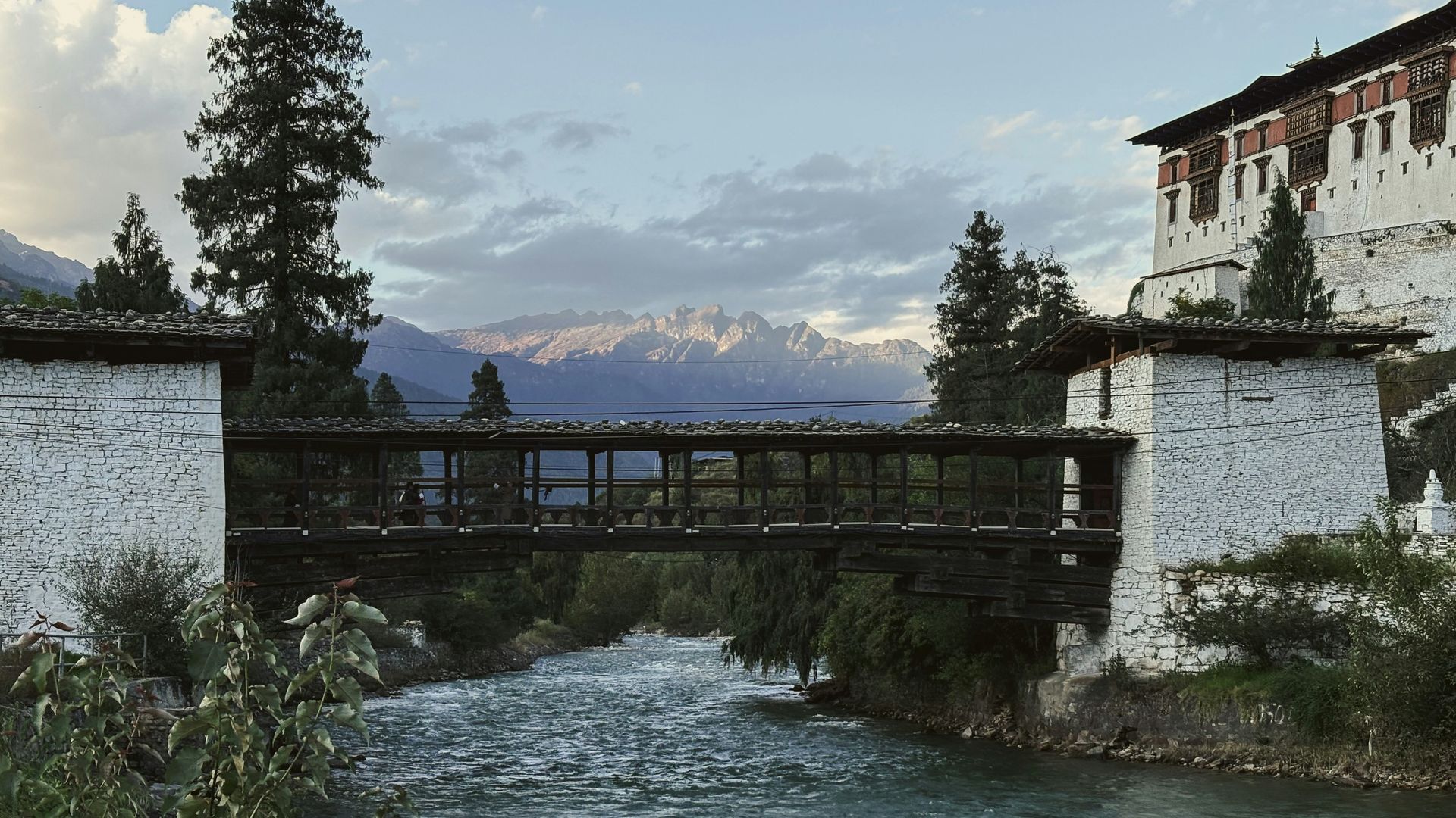 Covered bridge over a river, leading to Rinpung Dzong. Mountains in background in Paro, Bhutan.