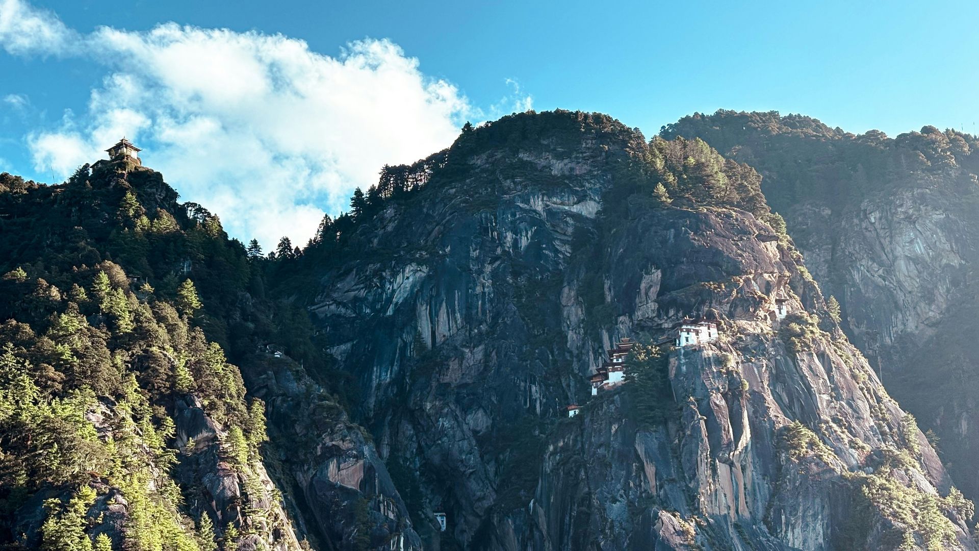 Mountainous landscape with green trees and Paro Taktsang perched on cliff in Bhutan.