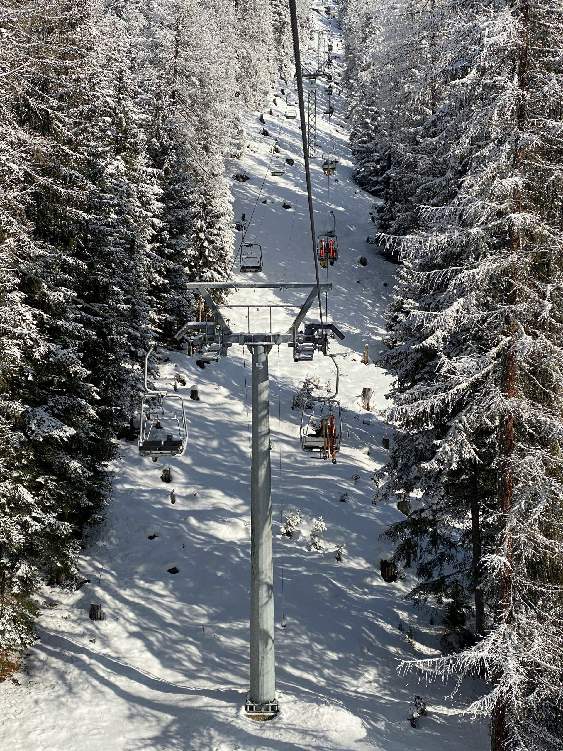 Ski lift ascends a snowy mountain, flanked by snow-covered evergreens in St. Moritz, Switzerland. 