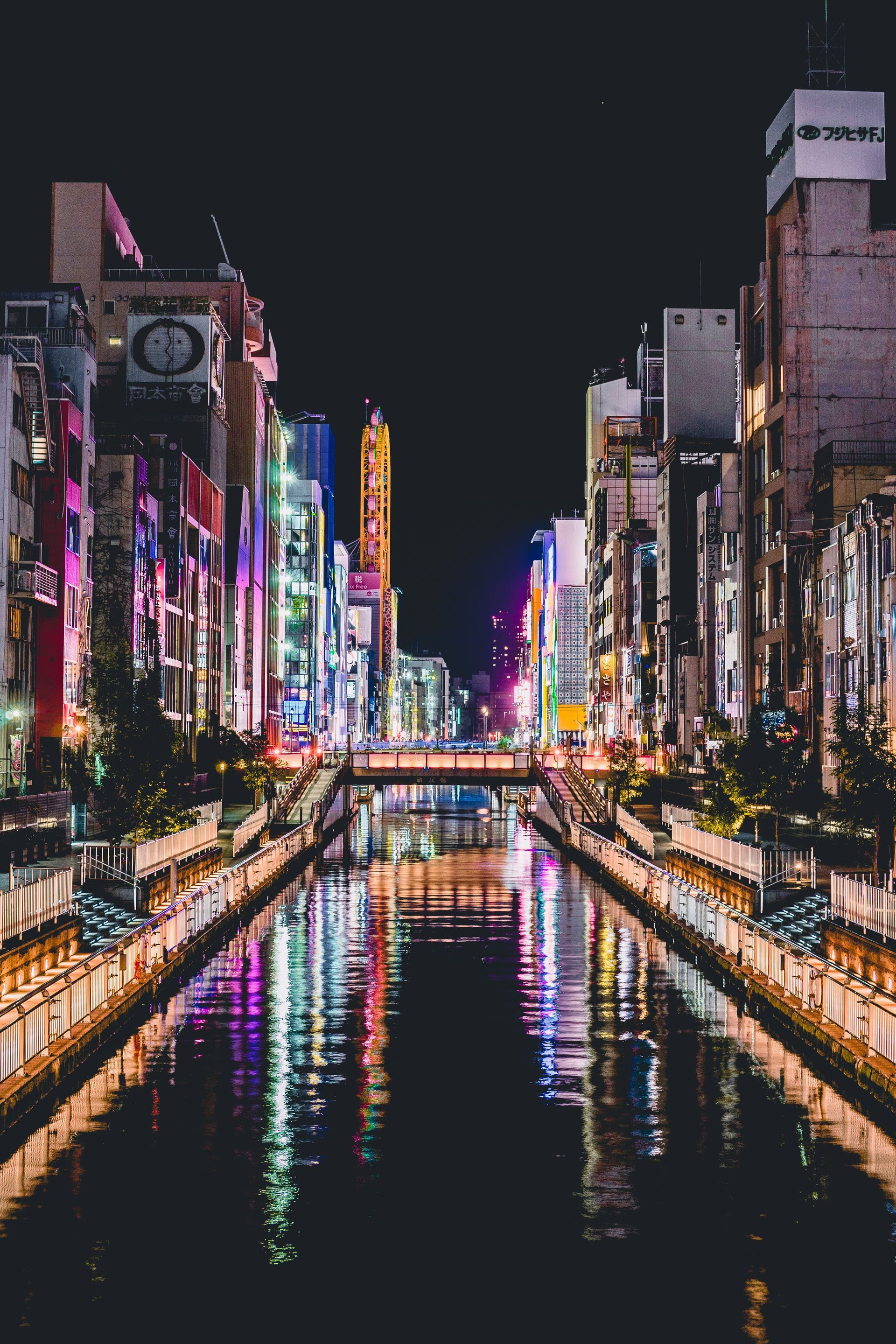 Cityscape at night; buildings with bright lights reflect in a river in Osaka, Japan.
