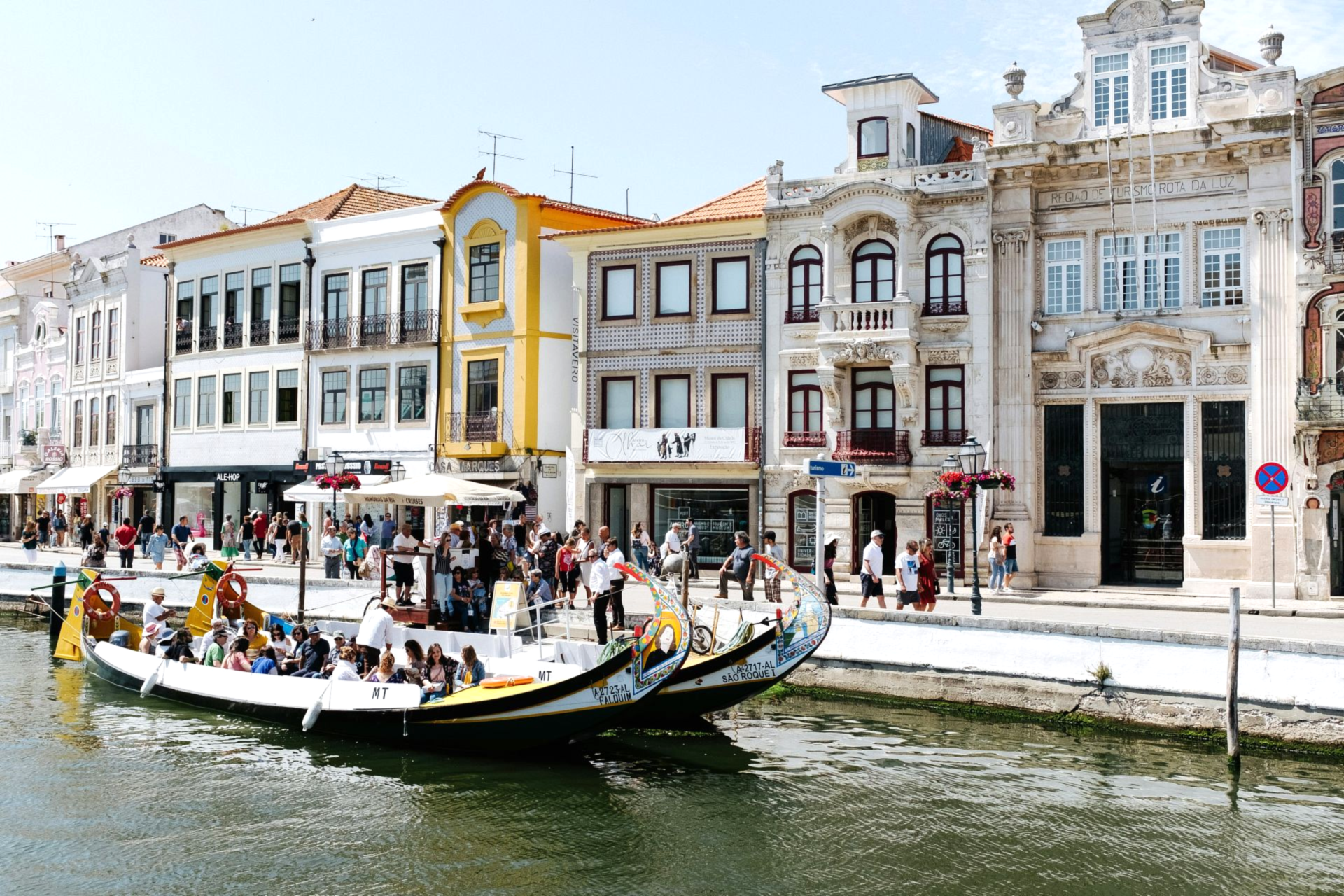 Canalside street scene in Aveiro, Portugal. Gondola boats with tourists. Pastel-colored buildings line the canal.