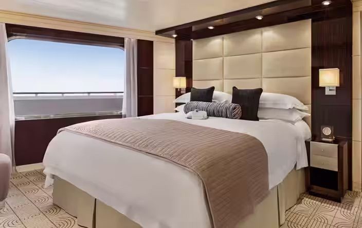 A hotel room with a large bed and a large window on the Oceania Marina cruise ship.