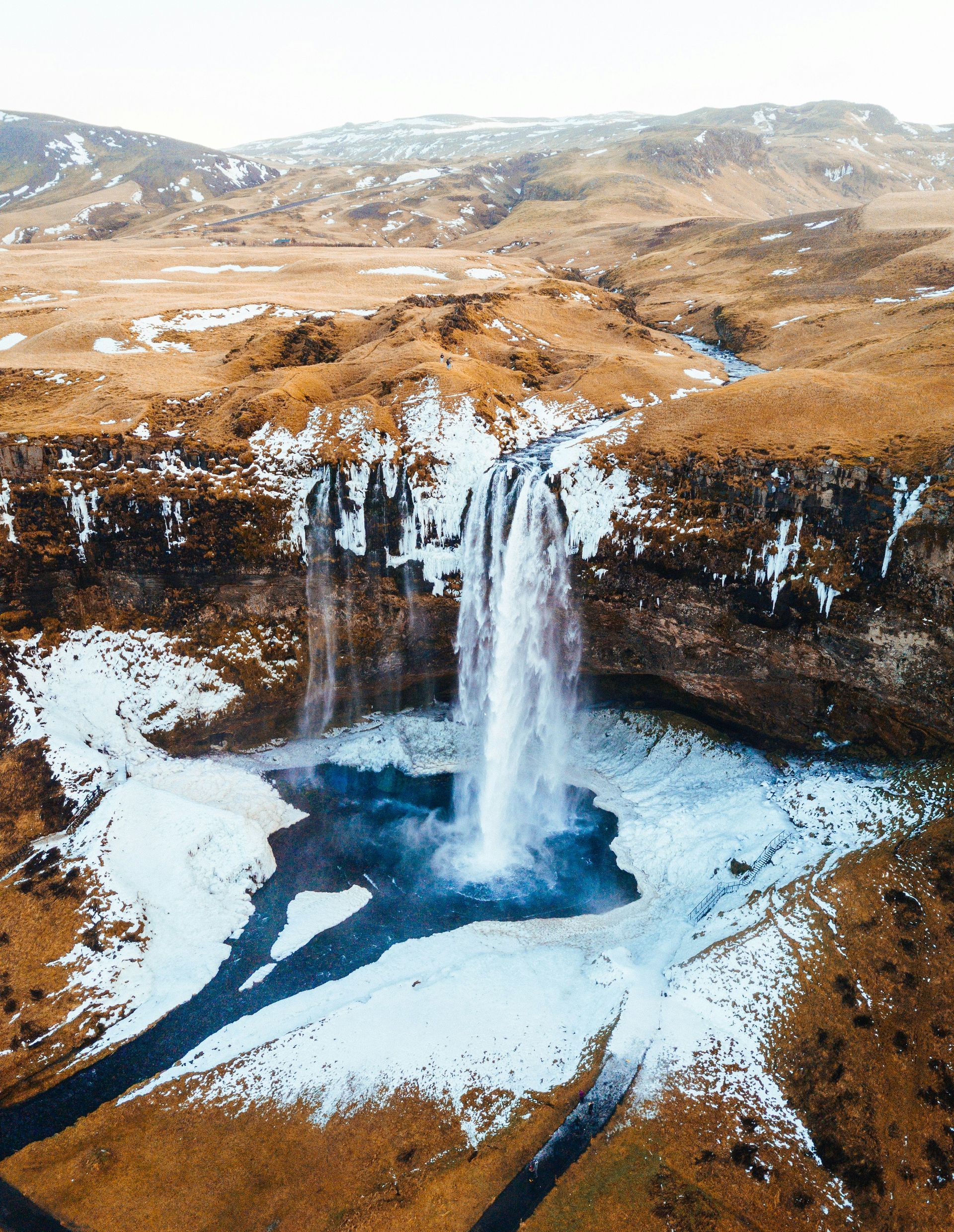 The Seljalandsfoss Waterfall cascading into a pool, surrounded by snow and brown, hilly landscape in Iceland.
