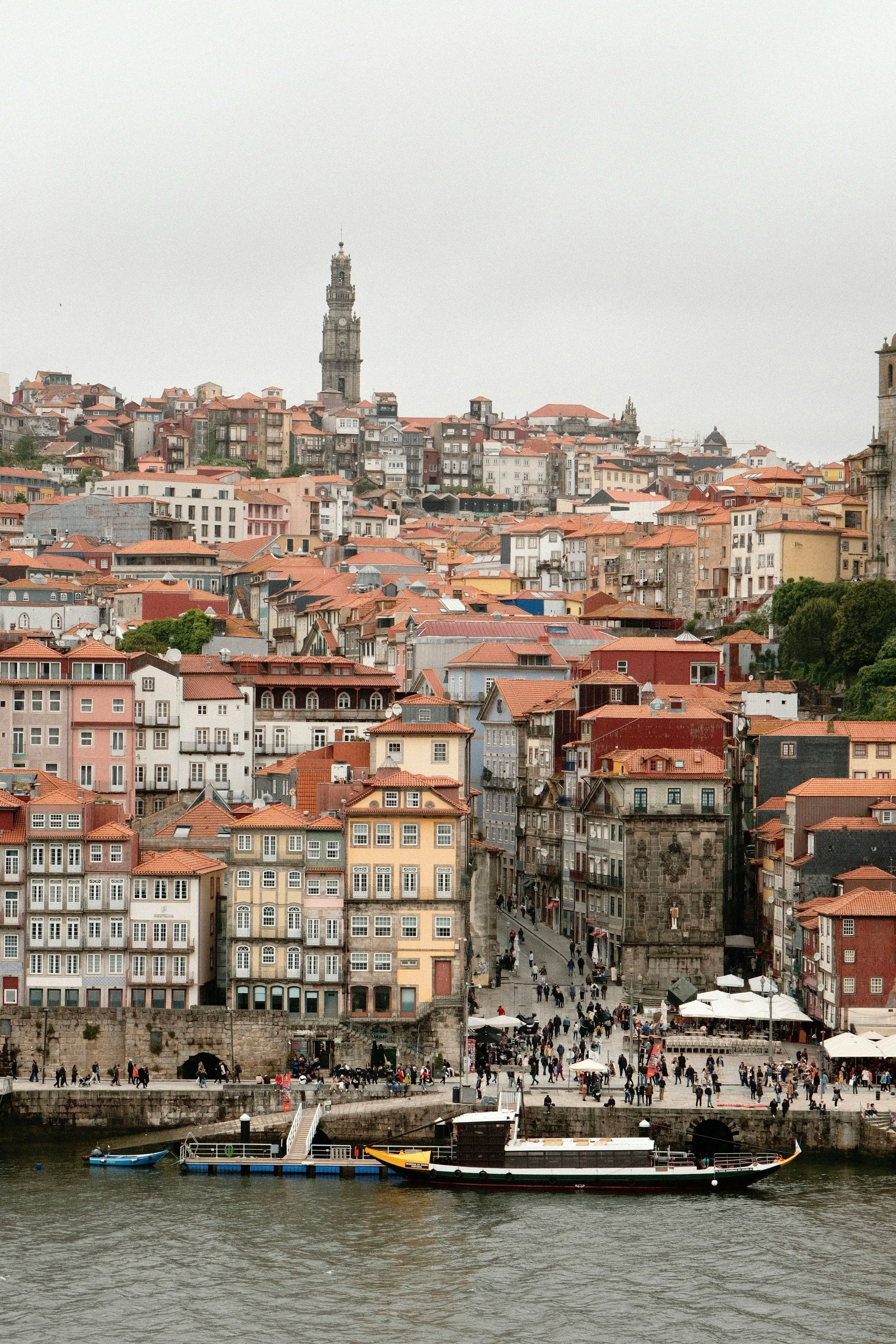 Porto cityscape with terracotta roofs and tower, people on riverside promenade.