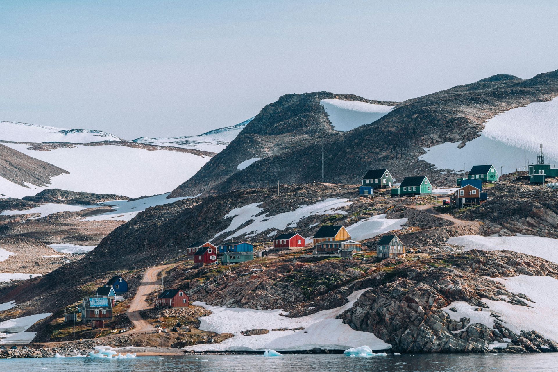 A small village is sitting on top of a snow-covered hill next to a body of water. in Greenland on HX Expedition Cruise.