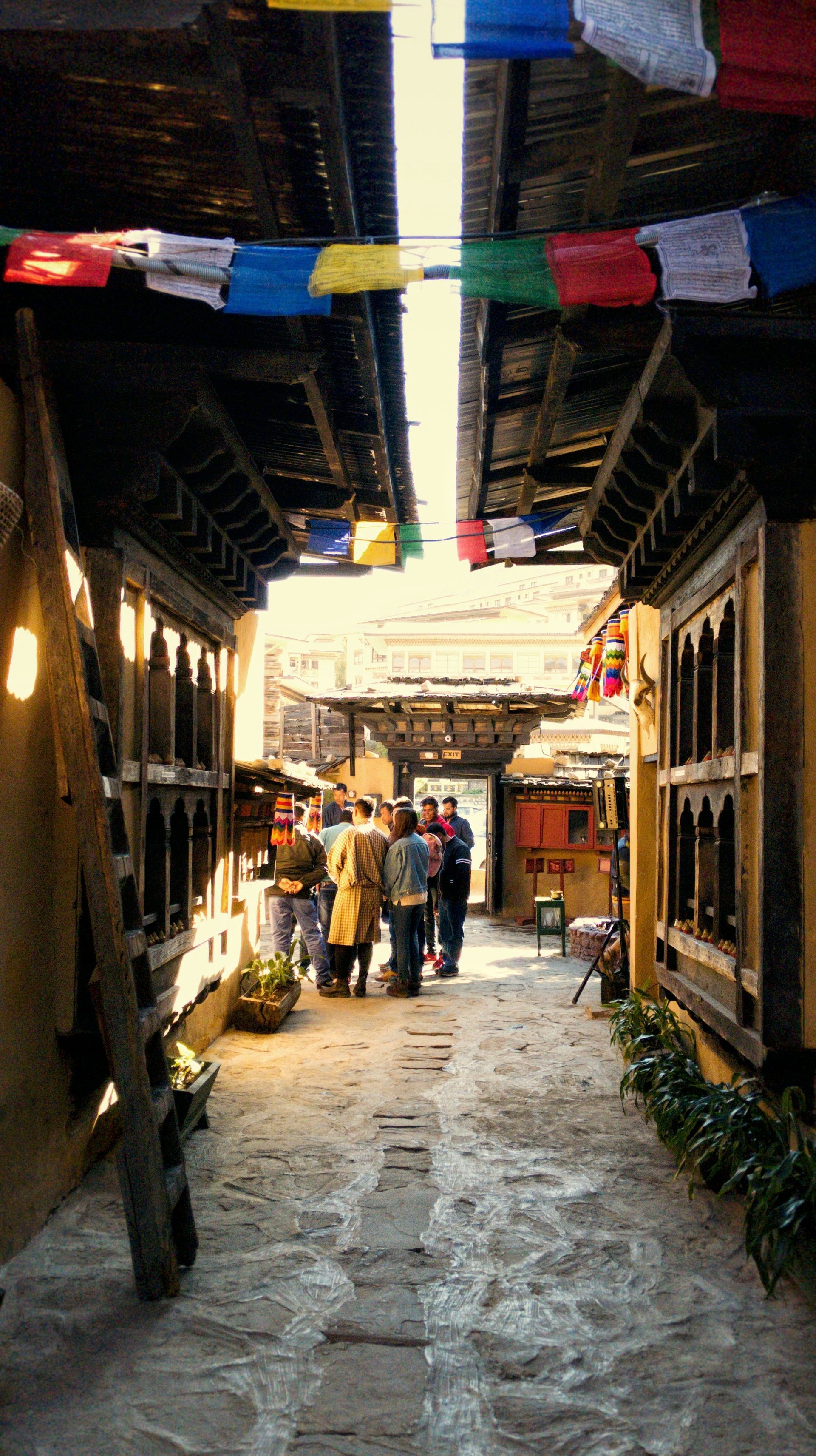 Narrow alleyway lined with buildings, colorful prayer flags overhead in Thimphu, Bhutan.