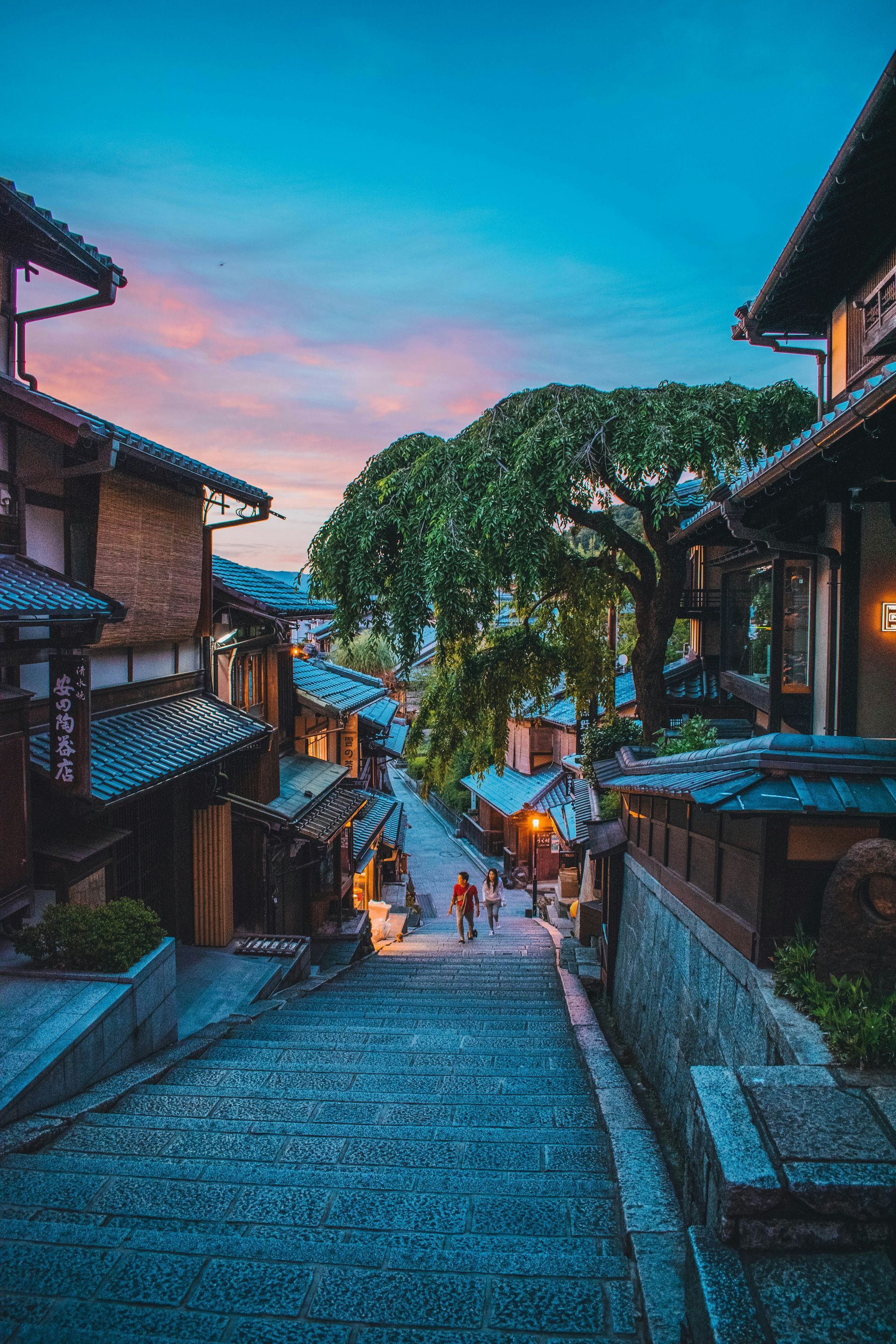 Stone street in Kyoto lined with wooden buildings at dusk, under a colorful sky.