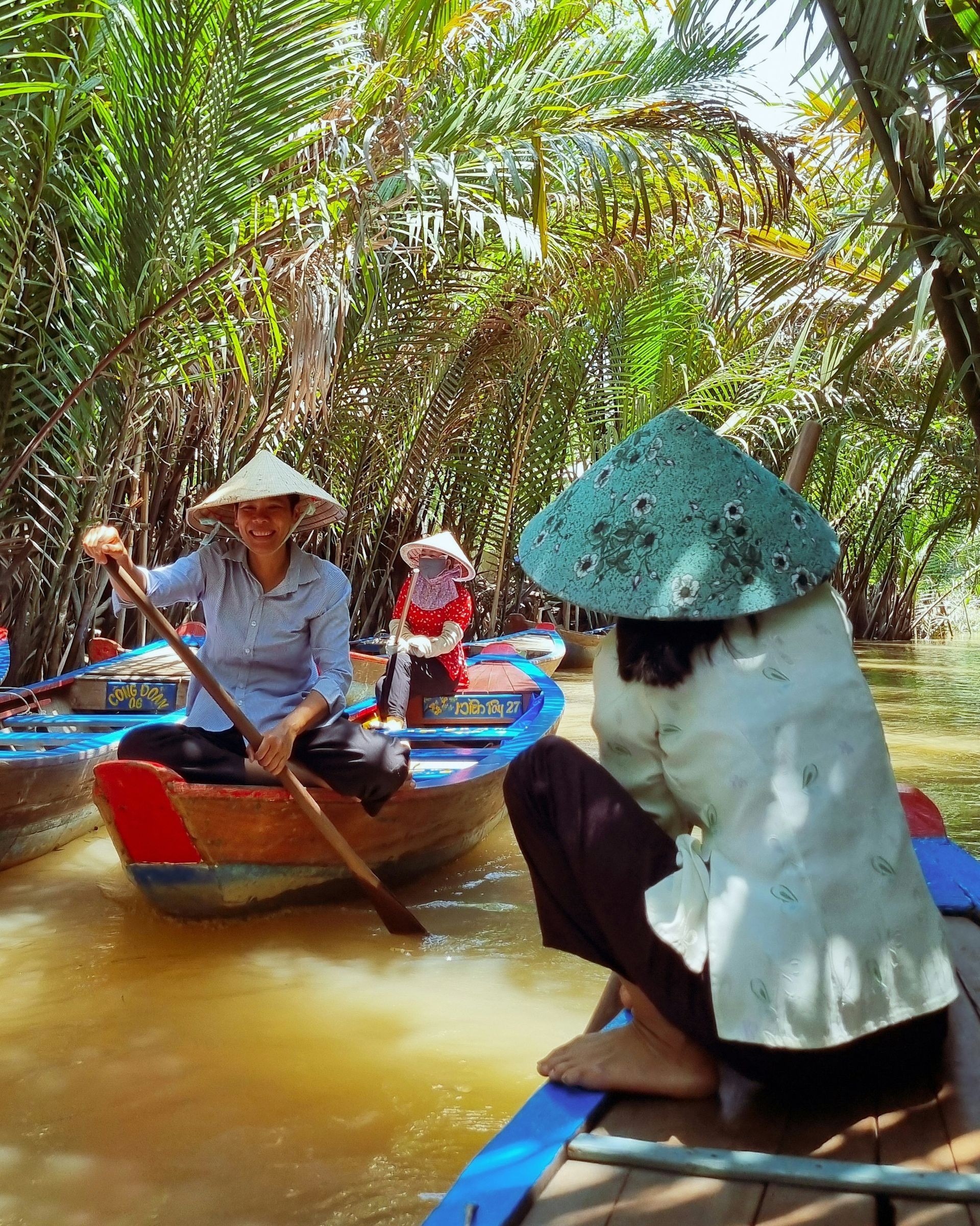 Women in conical hats rowing boats through the lush, green MenKong River.