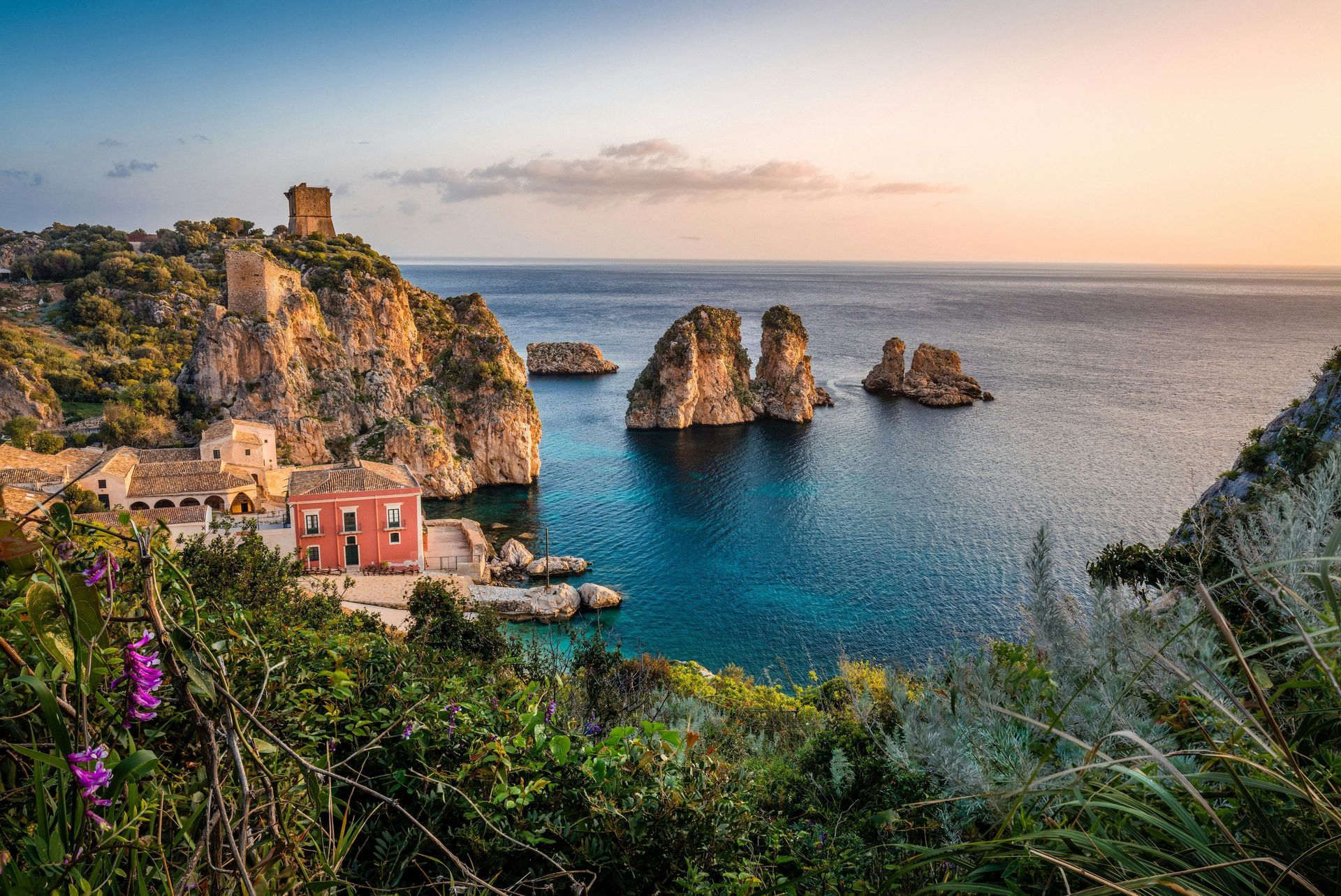 There are a lot of rocks in the water and a castle in the background in Sicily.