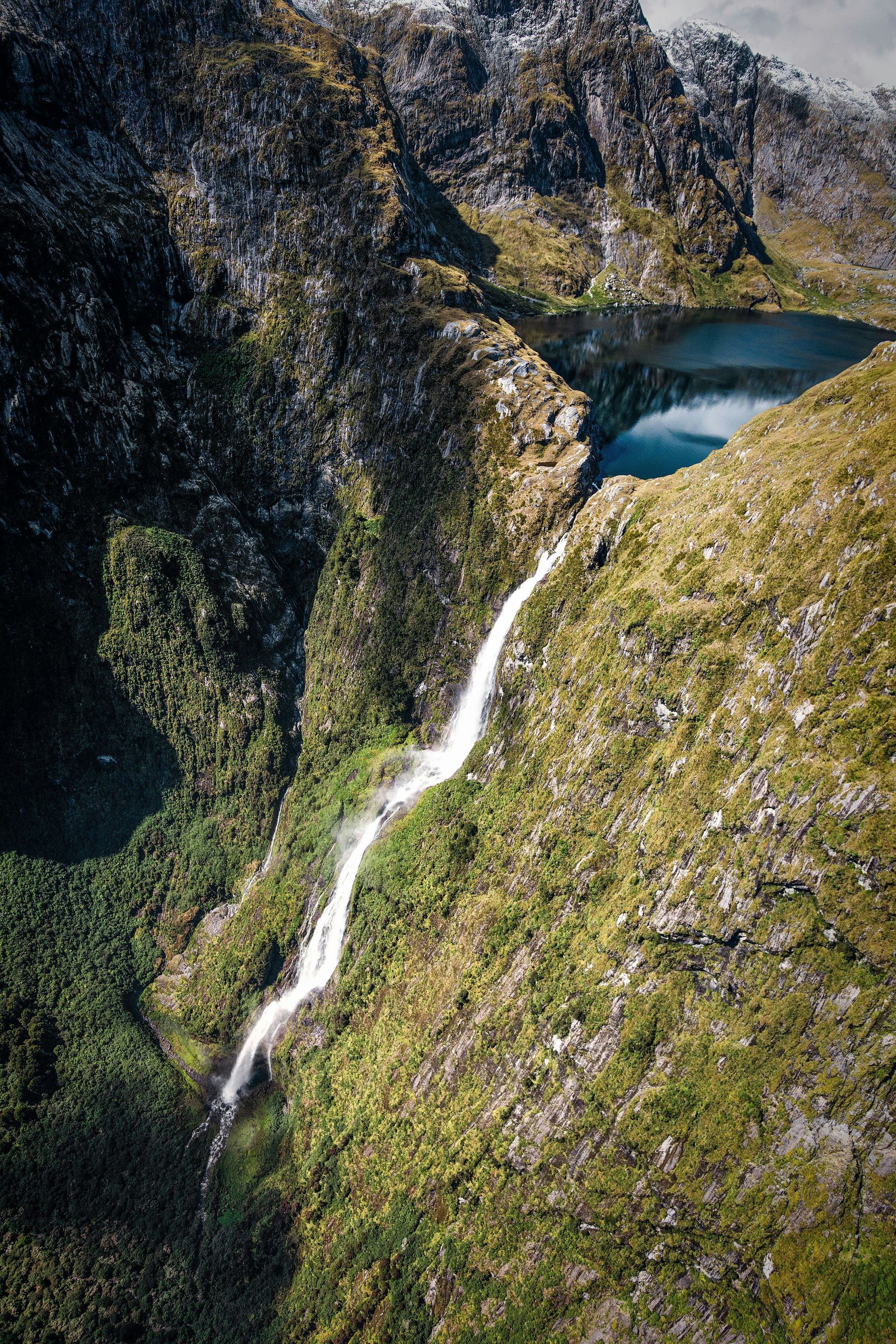 An aerial view of a waterfall in the middle of a mountain in Fiordland National Park, New Zealand.