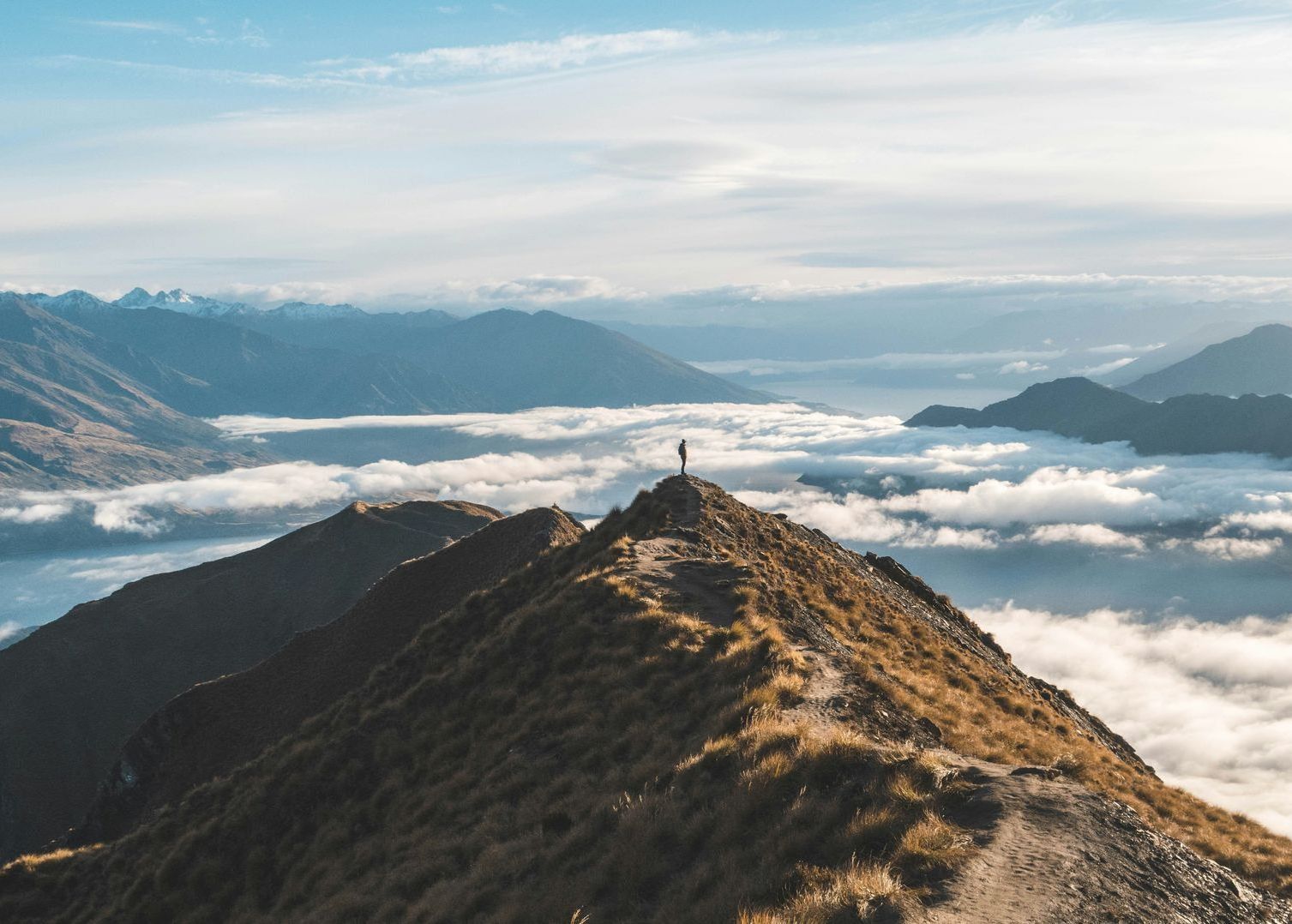 A person is standing on top of a mountain surrounded by clouds in Wānaka, New Zealand.