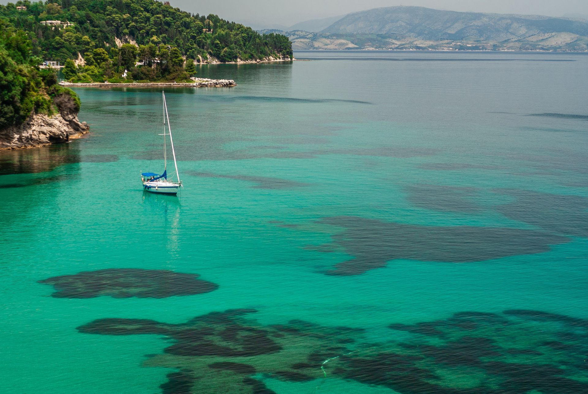 A sailboat is floating on top of a turquoise body of water in Corfu, Greece.