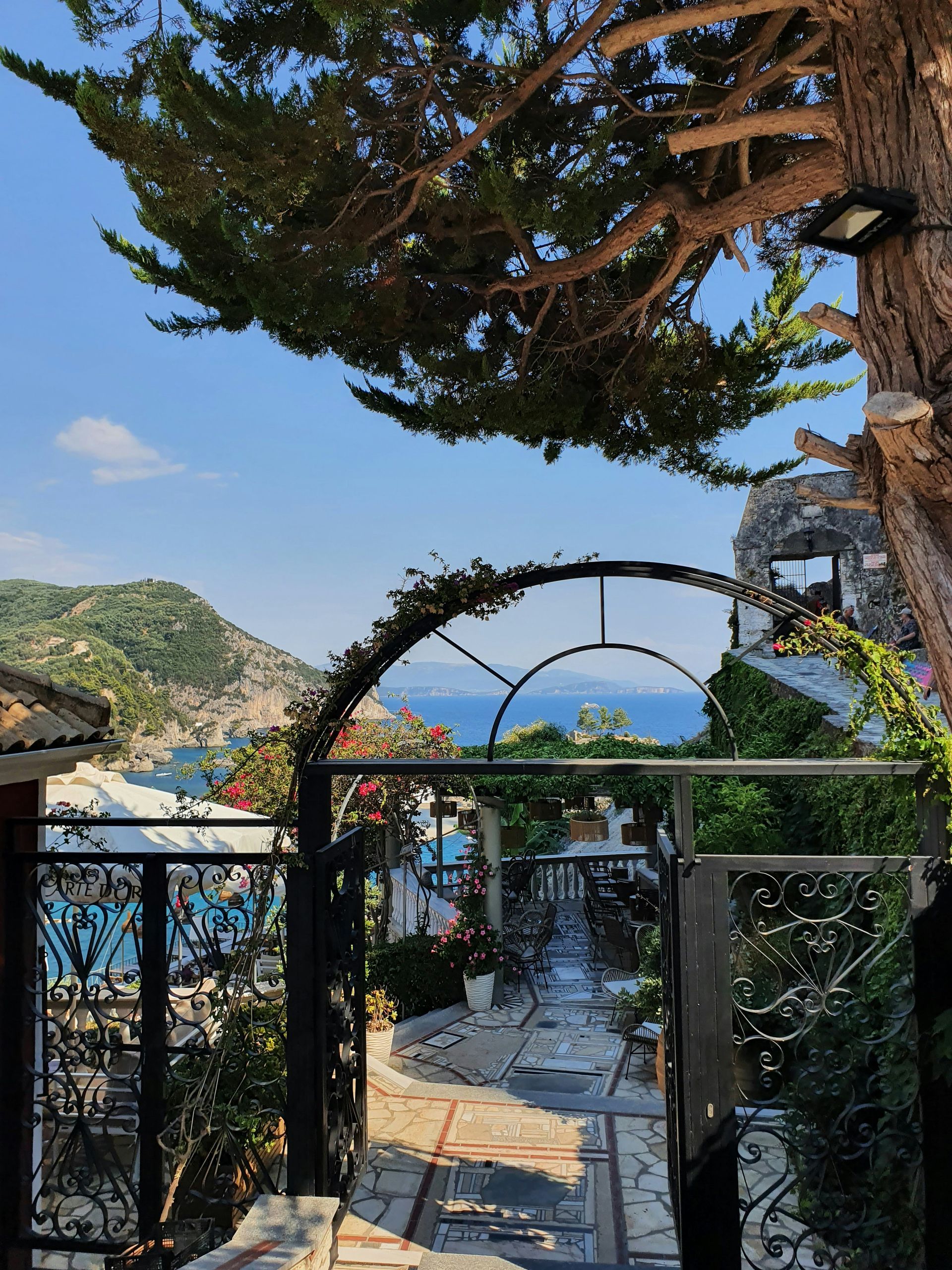 A view of the ocean through a gate with a tree in the foreground in Parga, Greece.