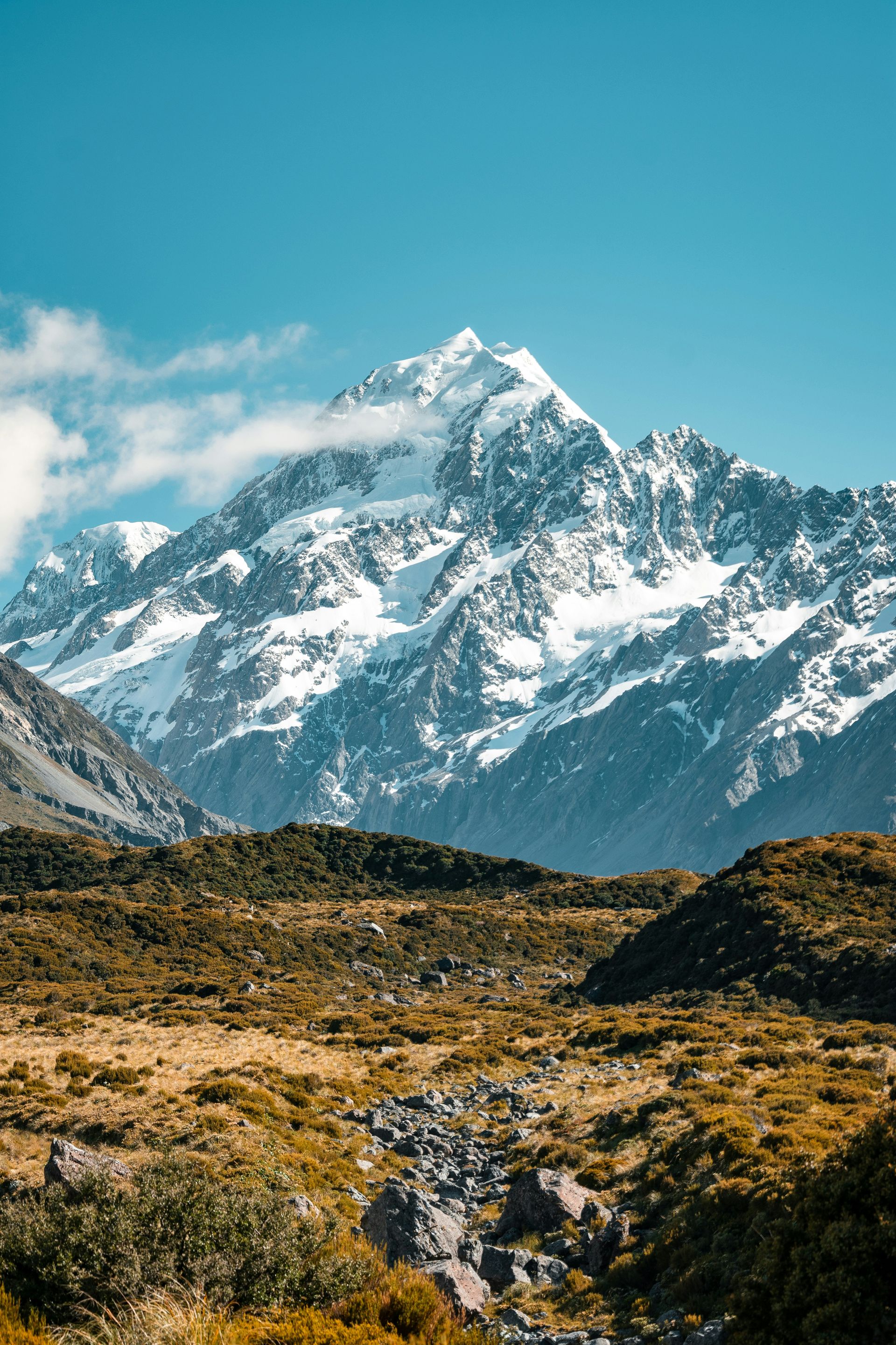 A snowy mountain covered in snow is surrounded by a grassy field in Mount Cook National Park, New Zealand.