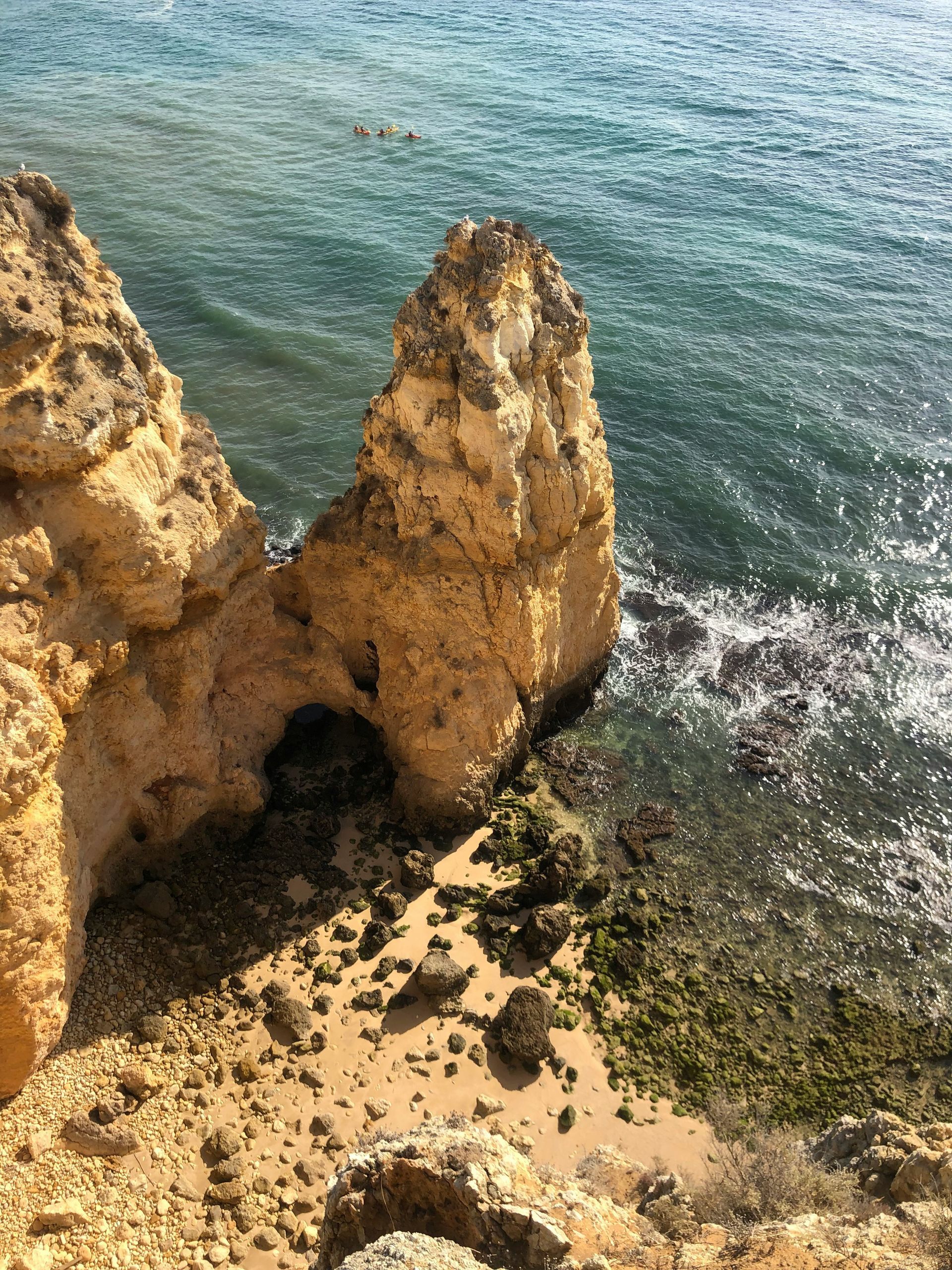 Rocky cliffs next to turquoise water with a small sea cave in Lagos, Portugal.