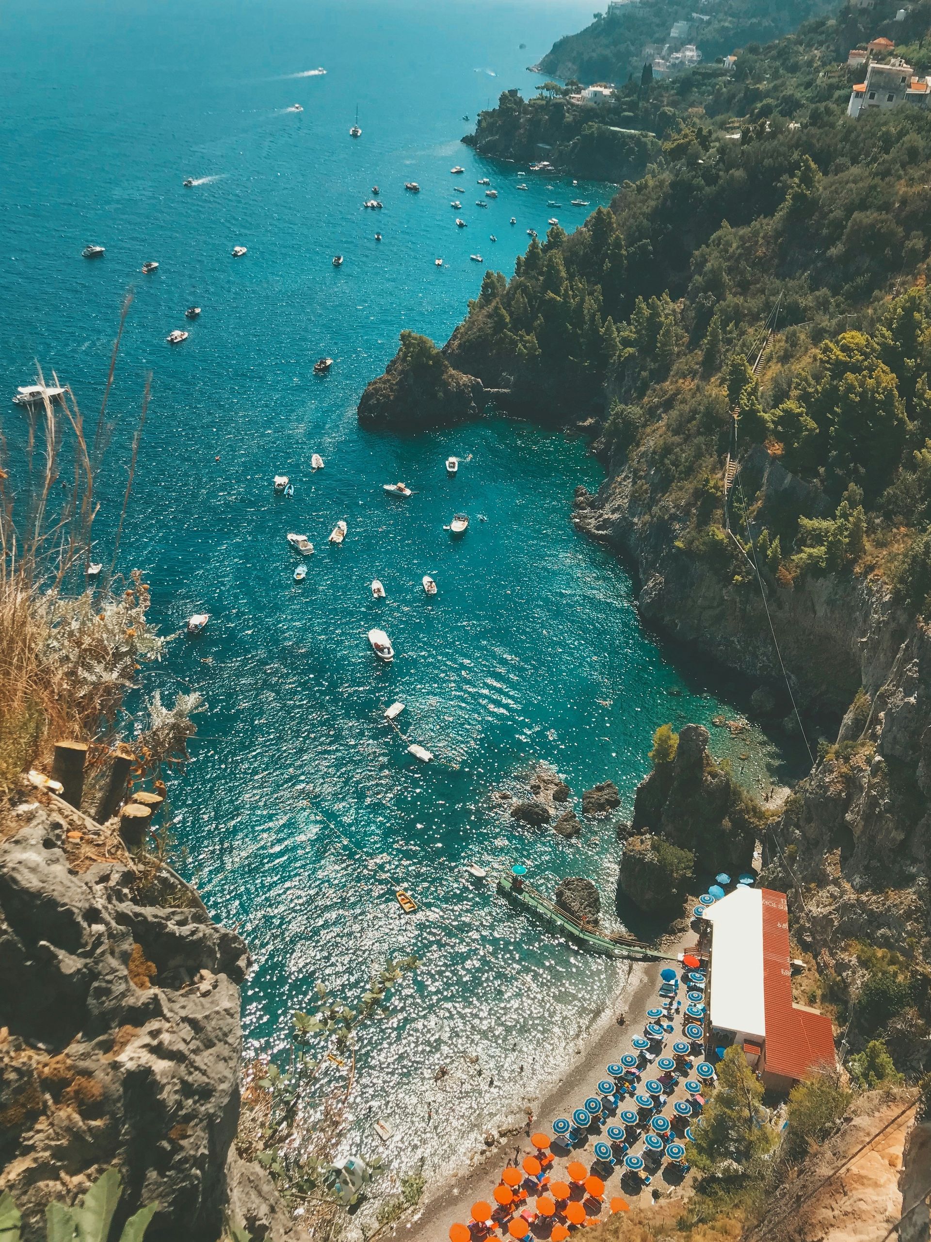 An aerial view of a cliff overlooking a body of water with boats in it on the Amalfi Coast.